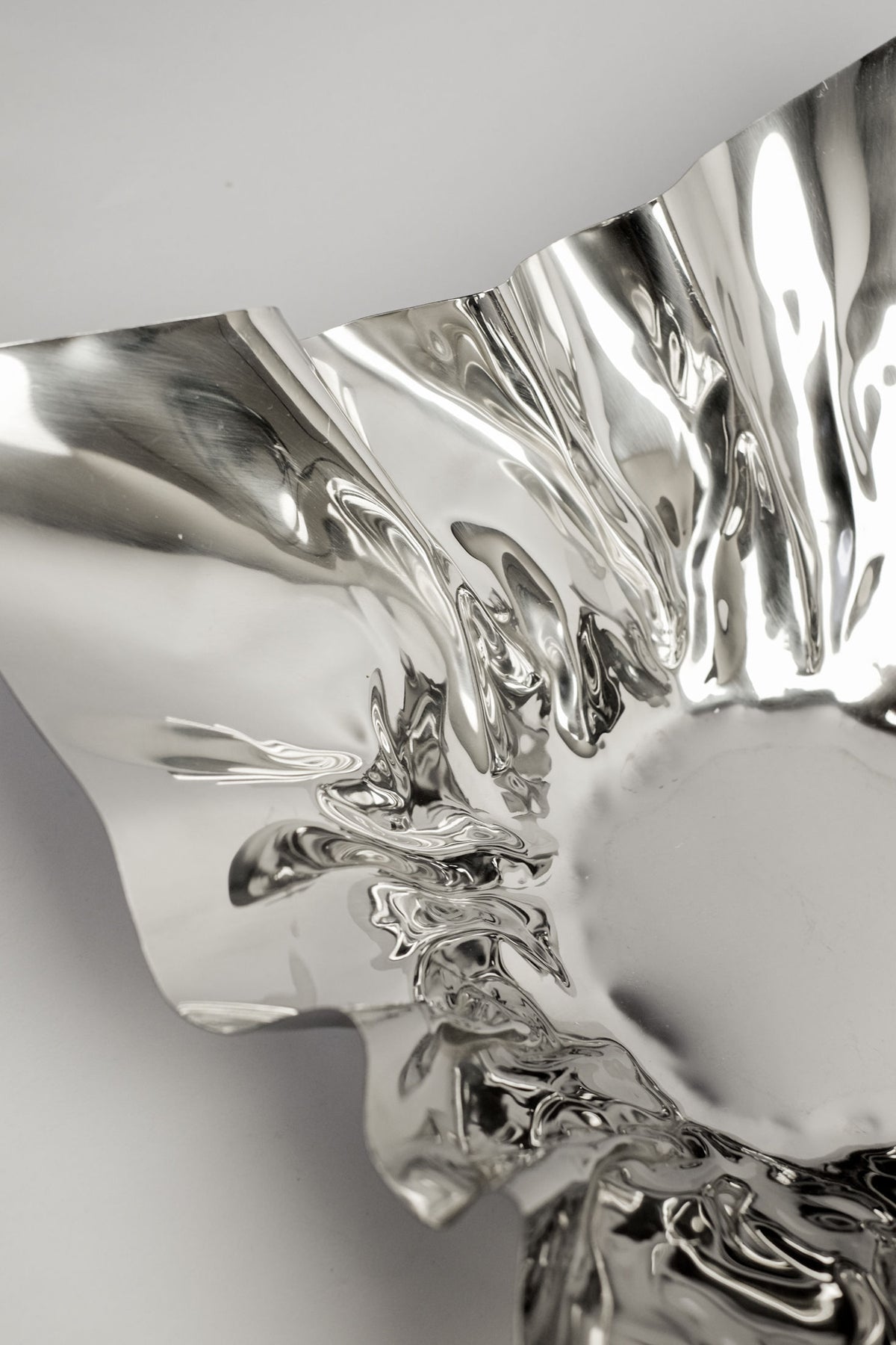 Close-up of the Extra Large Folded Chrome Bowl by septembre studios, featuring shiny, crumpled edges and reflective surfaces for an artistic, modern look—an eye-catching accent ideal for vintage-inspired interiors.