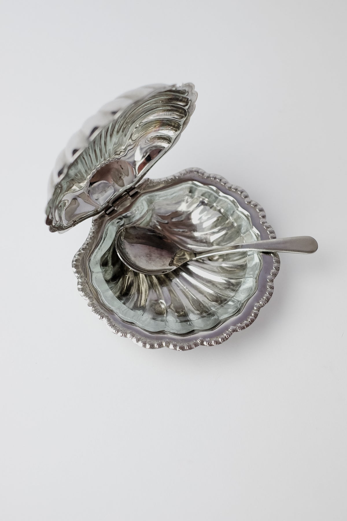 The Shell Shaped Butter Dish with Spoon by septembre studios features a vintage brass seashell design with an open lid and intricately scalloped edges. A small silver spoon rests inside, making this elegant dish ideal for enhancing any dining experience on a plain white surface.