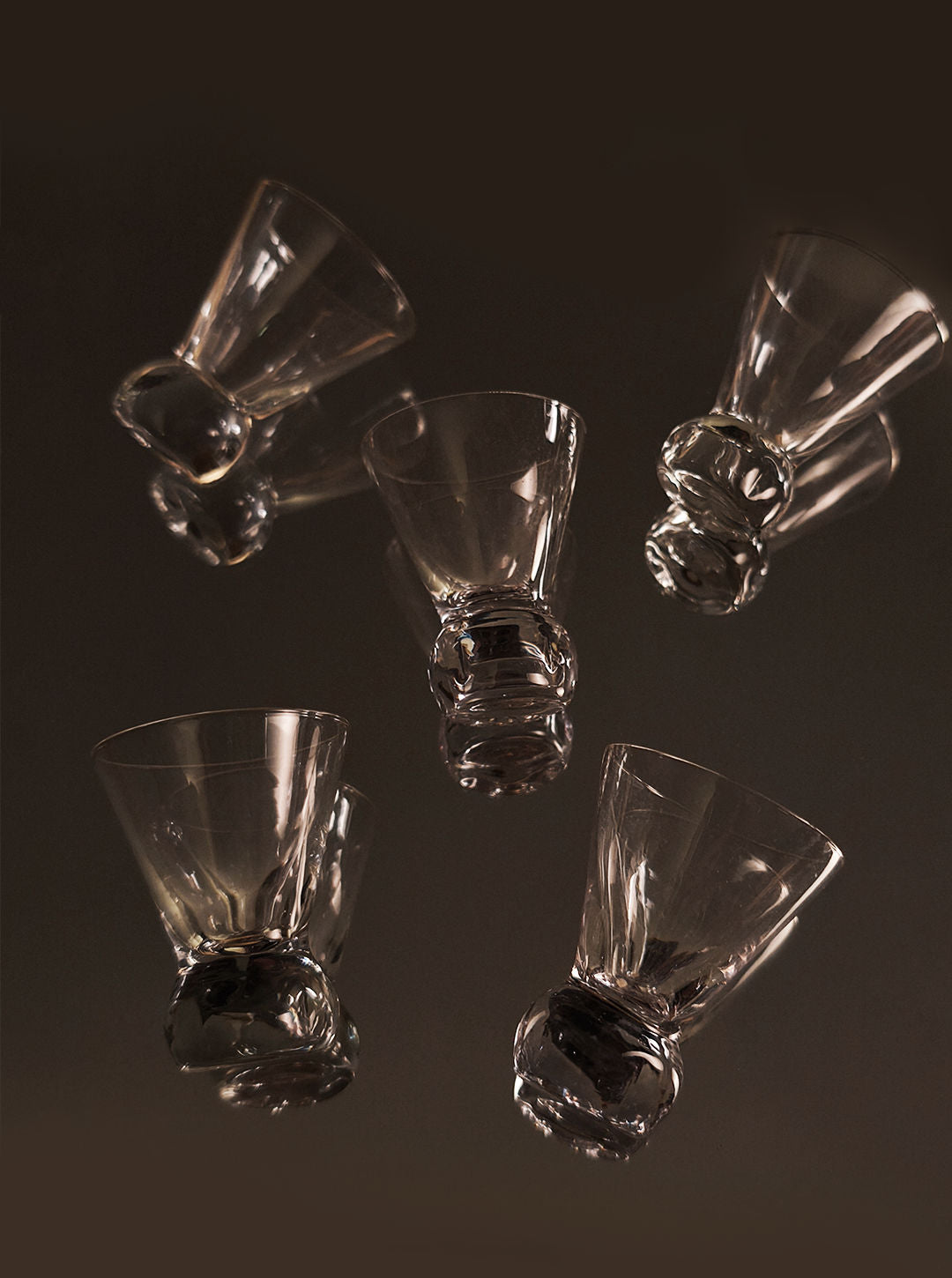 Five crystal shot glasses with twisted stems arranged on dark surface