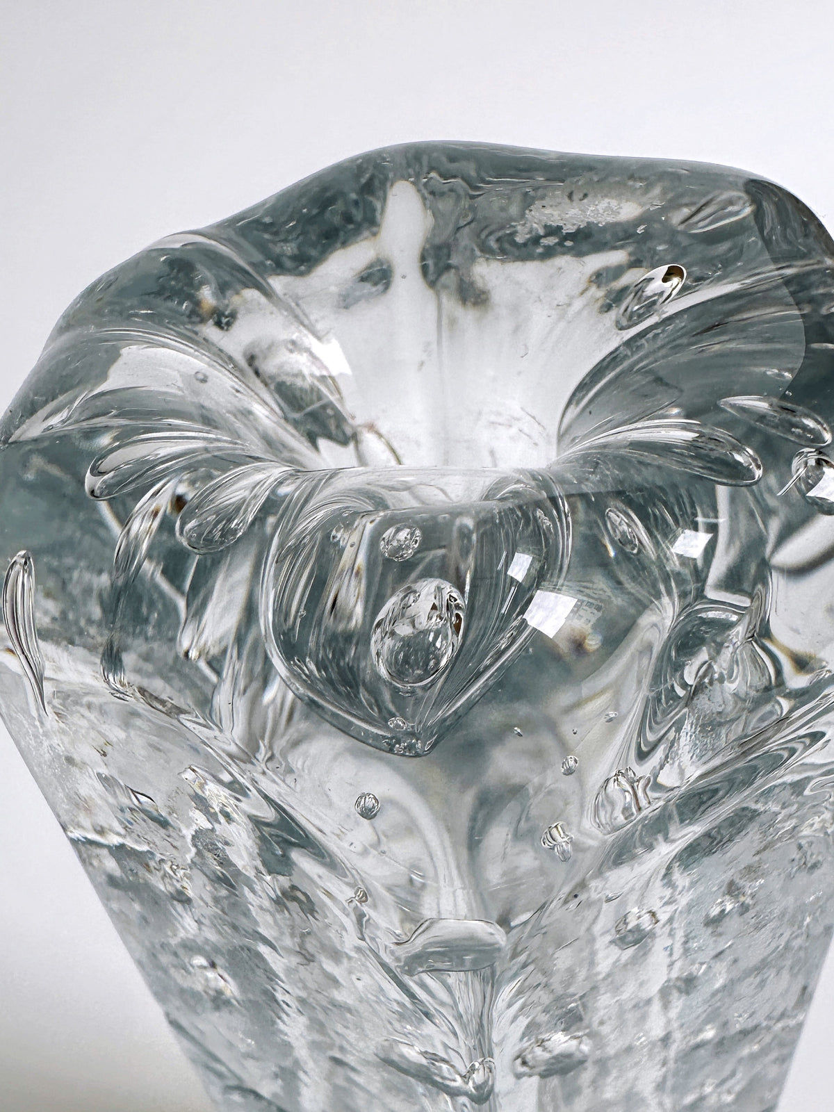 A close-up view of the 70s Swedish glass vase by Dodo Vintage showcases intricate internal patterns and bubbles. This piece features a smooth, slightly curved surface, creating a visually appealing play of reflections and refractions. The ice glass technique adds texture against the plain white background, making the details stand out.