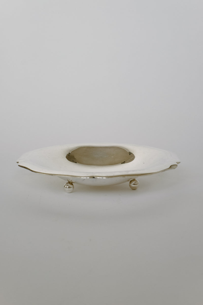 An elegant, oval-shaped Silverplated Bowl from septembre studios with a vintage charm and intricate detailing is placed against a simple background. The bowl is elevated on small decorative feet, and its gleaming surface reflects the light softly, bringing distinctive character to any environment.