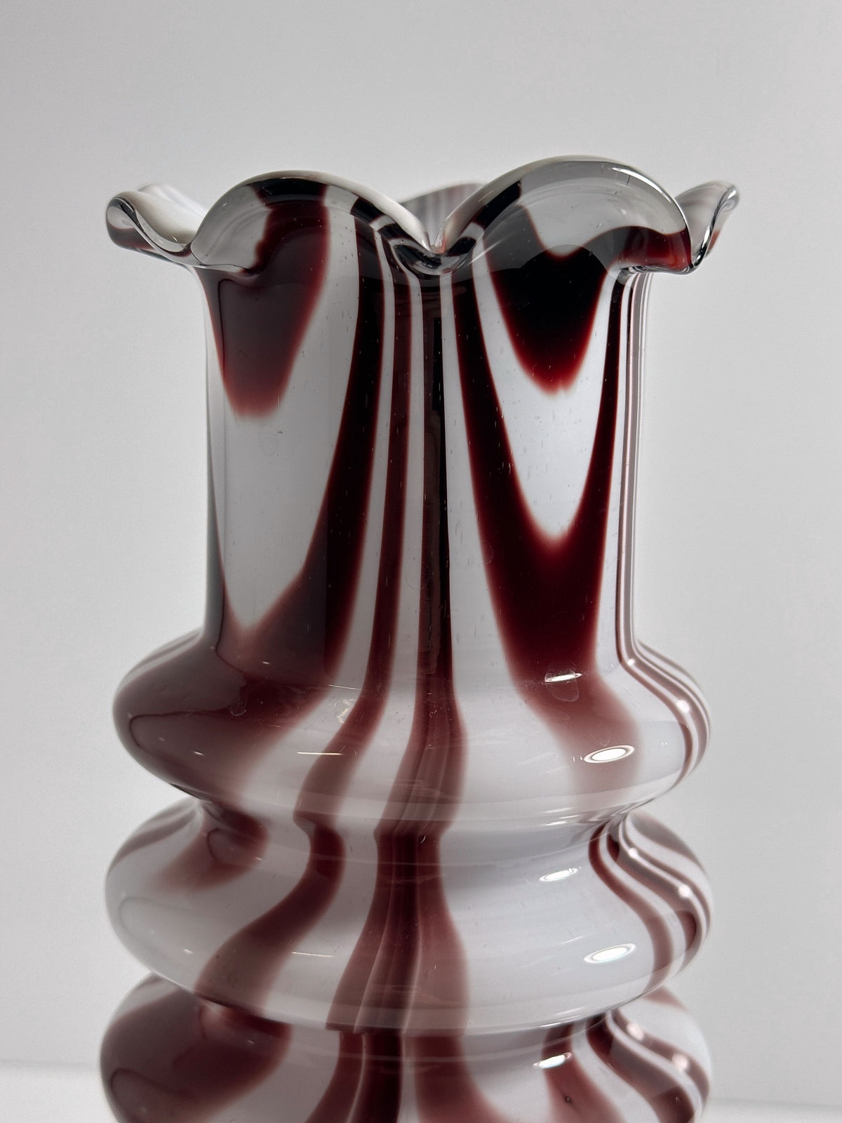 The 1970s Carlo Moretti Opalina Fiorentina Vase by Dodo Vintage boasts a wavy rim and elegant maroon-white swirls on a smooth opal glass body, creating a striking visual against a plain white backdrop.