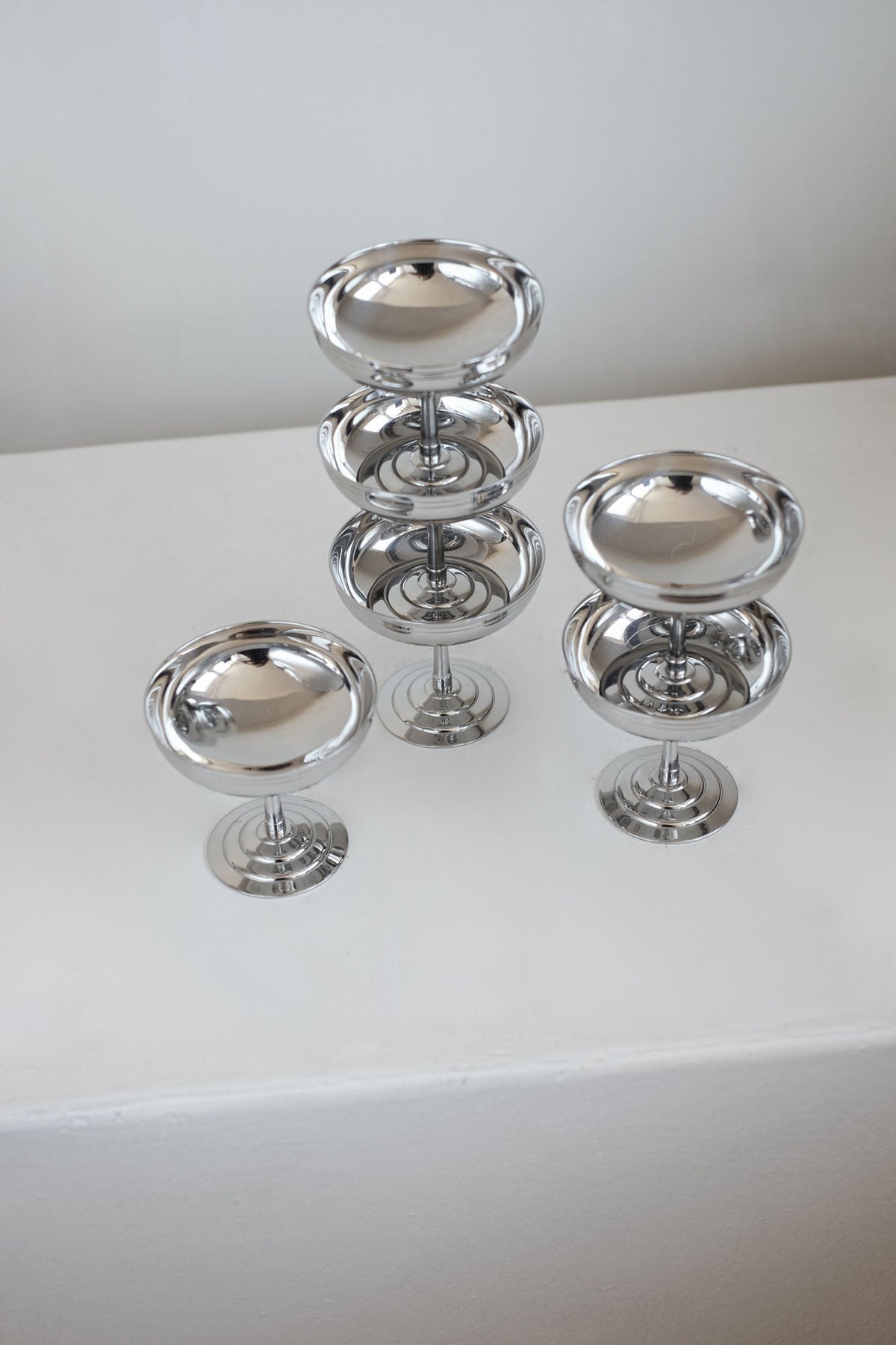 Set of 6 polished silver ice coupes stacked and arranged on white surface