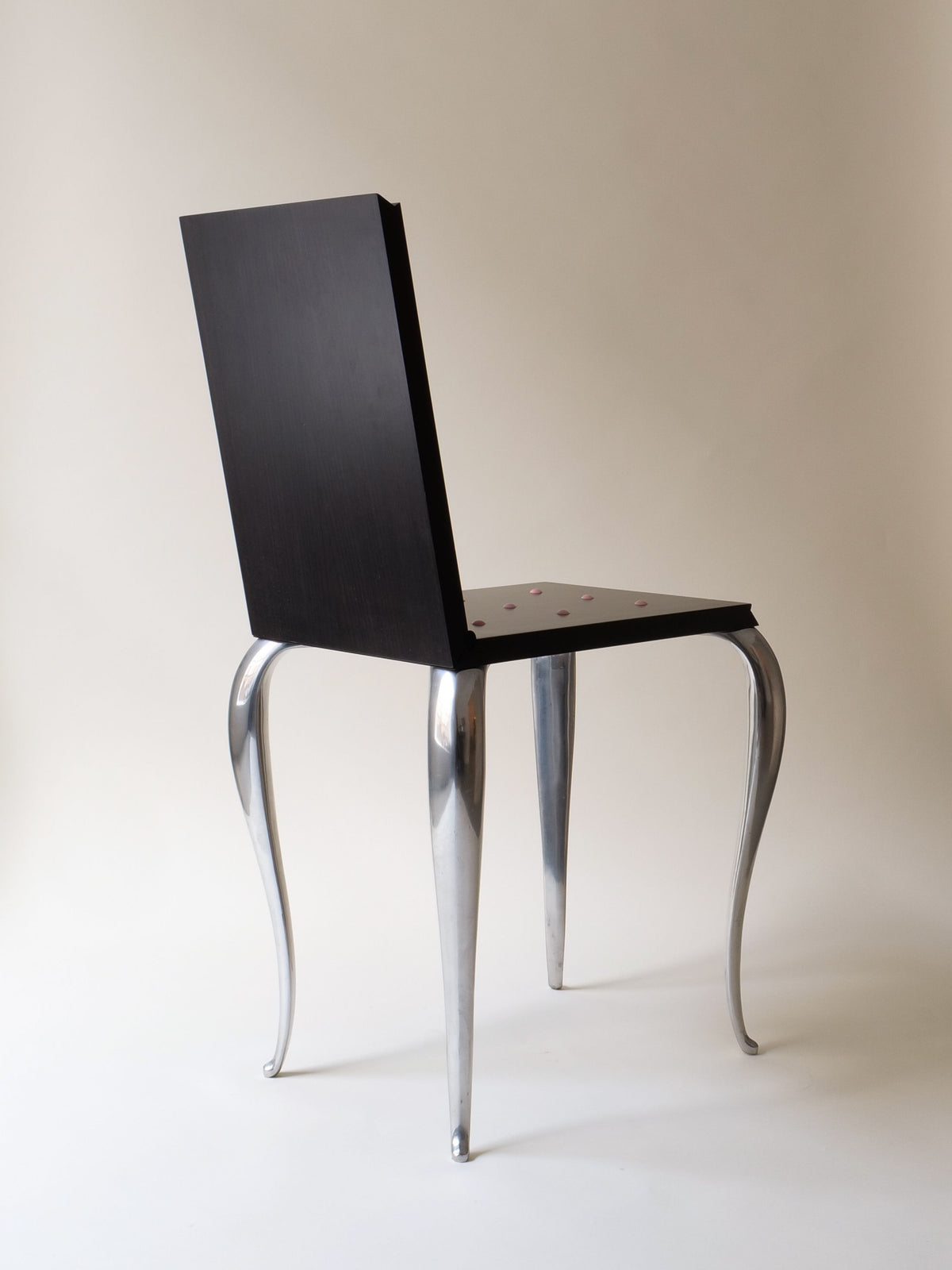 The "Lola Mundo Chair" by Philippe Starck (1984) from Collection apart boasts a sleek, dark wood backrest and seat with curved metallic legs, reminiscent of a modern design.