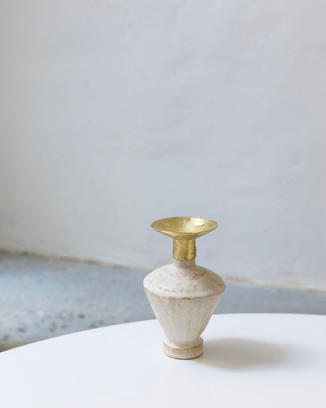 The Isolated n.6 Vase by Canoa Lab, featuring white textured ceramic inspired by Mediterranean design and a wide gold metallic rim, rests on a round white surface against a plain light gray background.