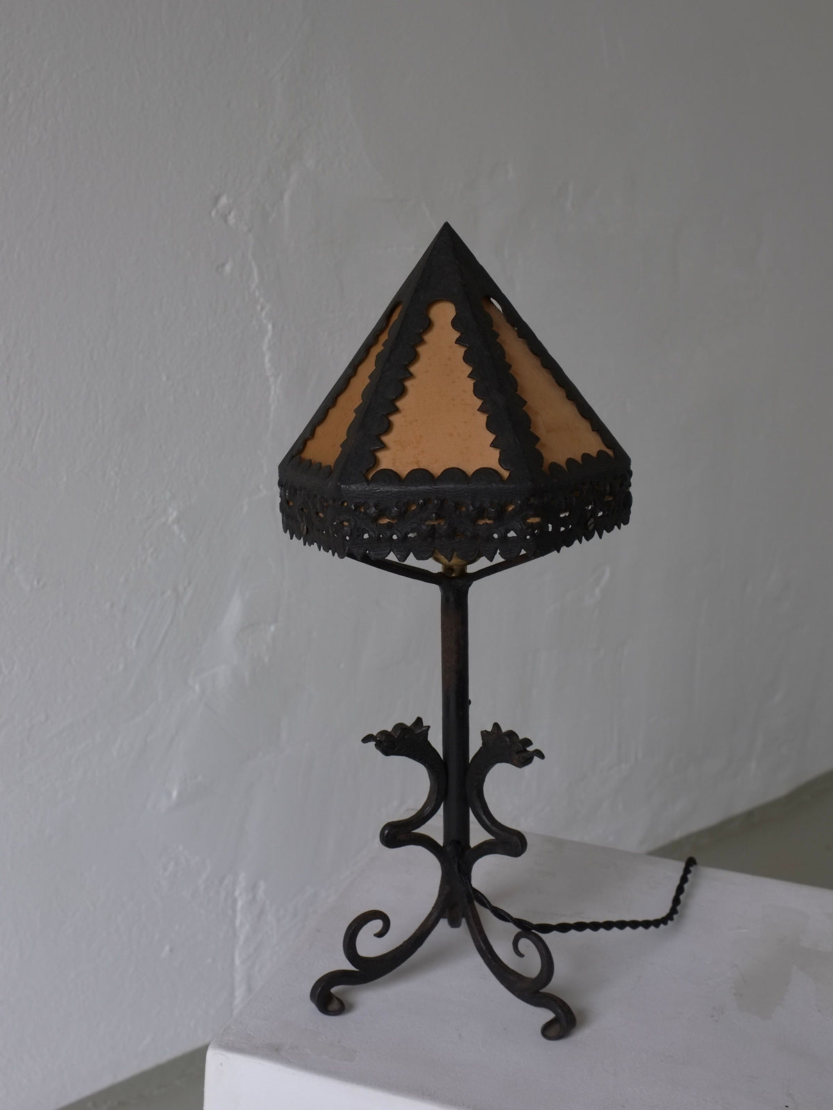 The Veter Vintage Wrought Iron Dragon Table Lamp, Italy 1910s, featuring a scalloped brown and black silk shade and ornate black metal base, sits on a white pedestal against a plain light gray wall.