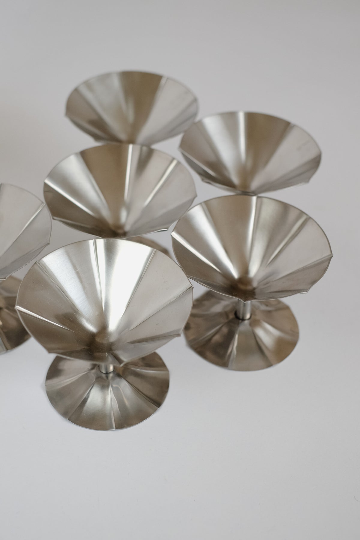 A cluster of six metallic, cone-shaped ice coupes from septembre studios, each with a folded, fan-like design, rests elegantly on a light surface.
