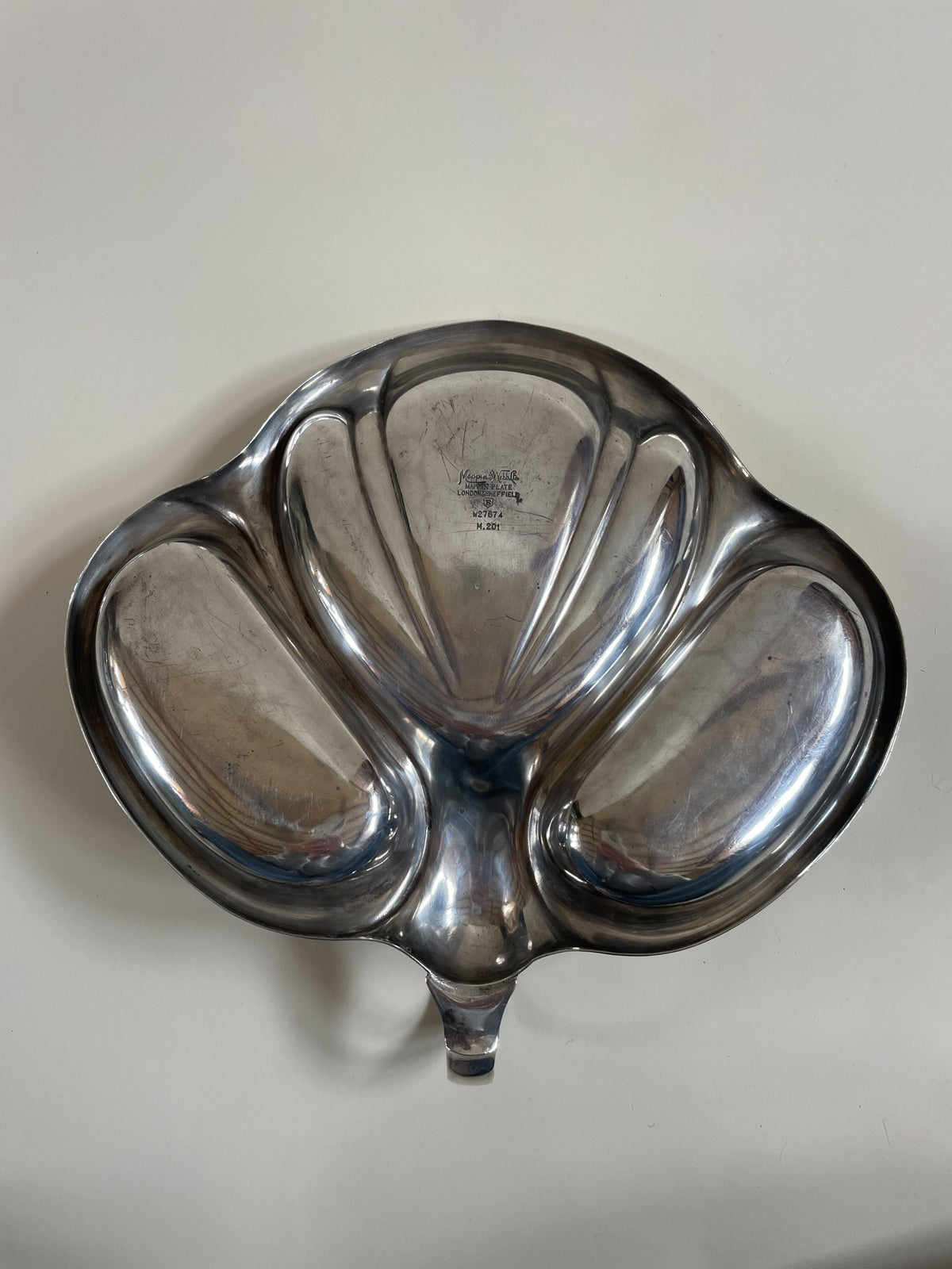 A Vintage Mappin and Webb Silver Plate Serving Dish by Maud Vaughan with five separate compartments, designed in an organic shape resembling petals. The surface appears polished and reflective, with a central stamp detailing Mappin and Webb's information. This smart serving dish rests against a plain, light-colored background.