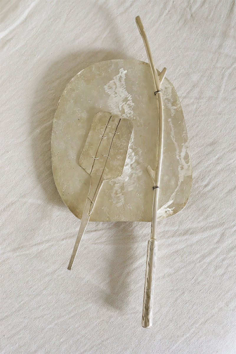 A delicately crafted Silver Plated Cake Server by Rooms Studio lies on a textured white fabric. The server has an organic, asymmetrical shape and features a slender handle with a flat, rectangular scoop. This set, reminiscent of Tbilisi Georgia's artisanal charm, exudes elegance.