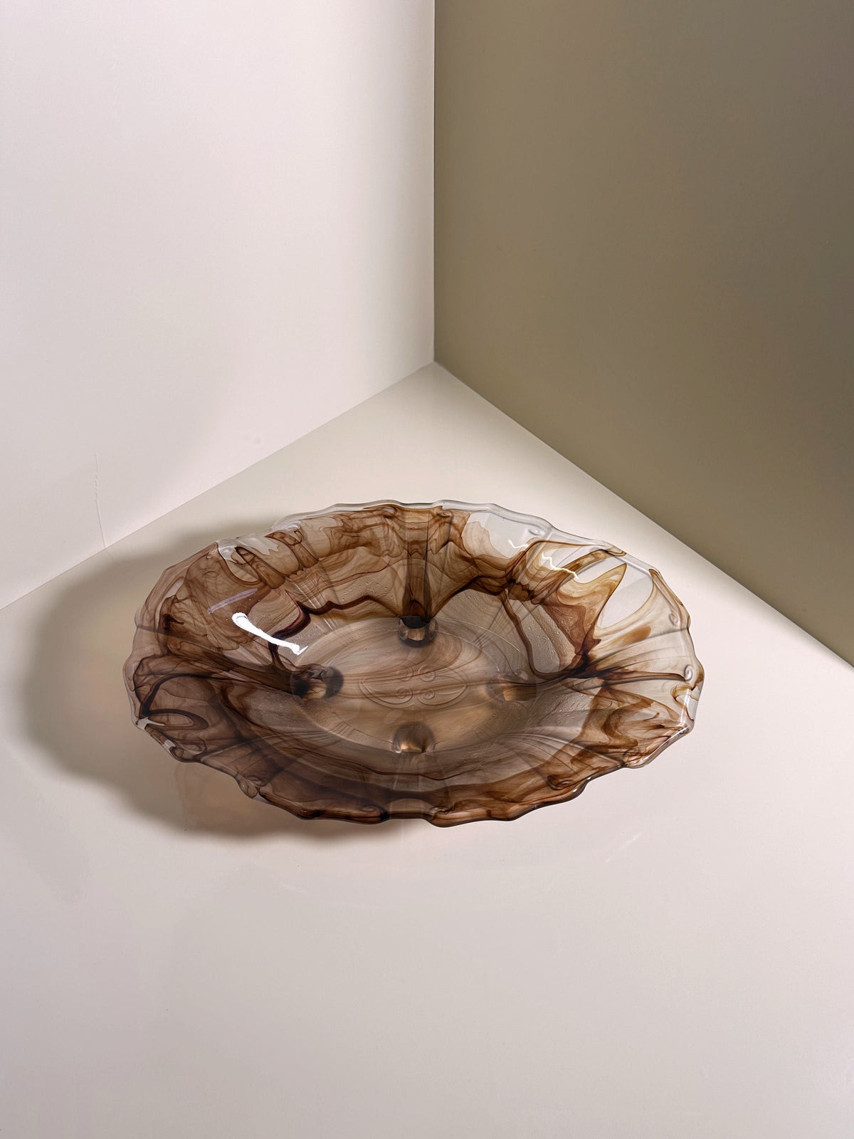 The German Art Deco Cloud Glass Bowl circa 1930 by Dodo Vintage features translucent glass with brown swirls and wavy edges, sitting on a white surface in the corner where two light gray walls meet, casting a delicate shadow.