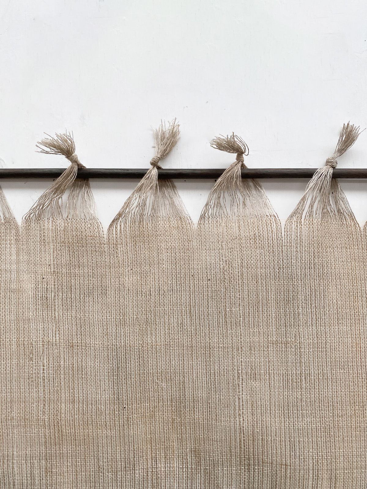 The Sundance Studio's Distant Horizon is a beige woven curtain with knotted fringes at the top, hanging from a dark metal rod and evoking the expansive open spaces and natural beauty of Yuraygir National Park on Yaegl Country.