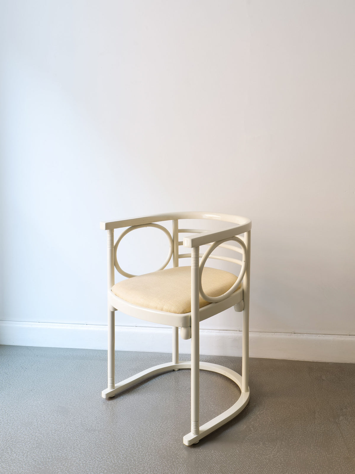 A Thonet Bentwood Chair by Josef Hoffman from the Collection apart brand, featuring a modern design with a circular backrest and upholstered seat in beige, rests on a light gray floor against a plain white wall.