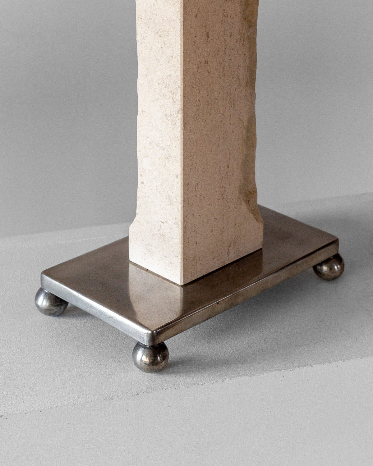 The Spigel Modernist Travertine and Metal Table Lamp features a rectangular pillar in Art Deco style on a metal base with four rounded feet, sitting on a smooth, light surface against a gradient light gray background.