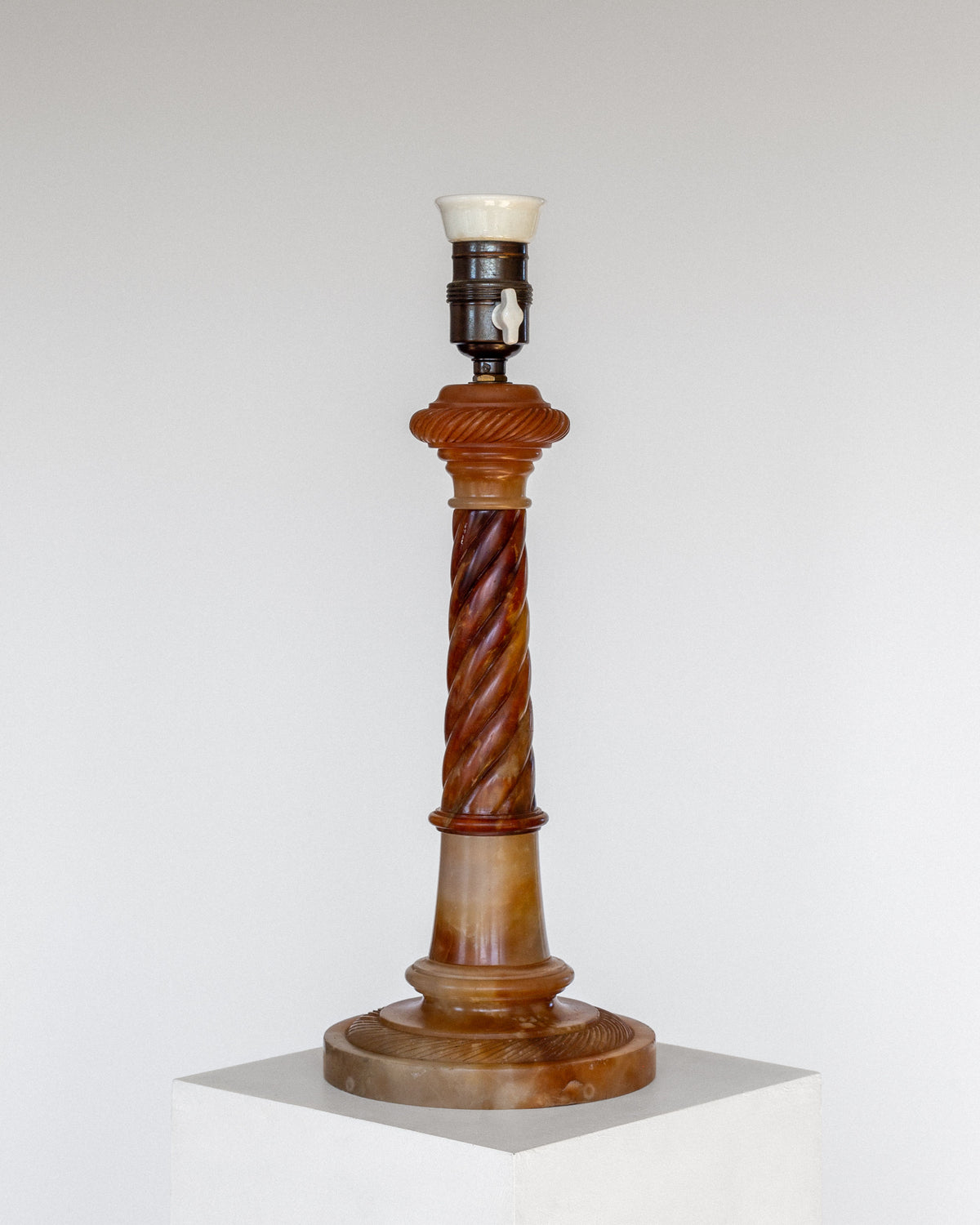 The Spigel Antique Alabaster Table Lamp, C. 1900, boasts a vintage ceramic lamp base with a twisted column design in shades of brown and beige. It is set atop a hand-carved alabaster base against a plain background. Please note that the lamp is missing its shade and bulb.