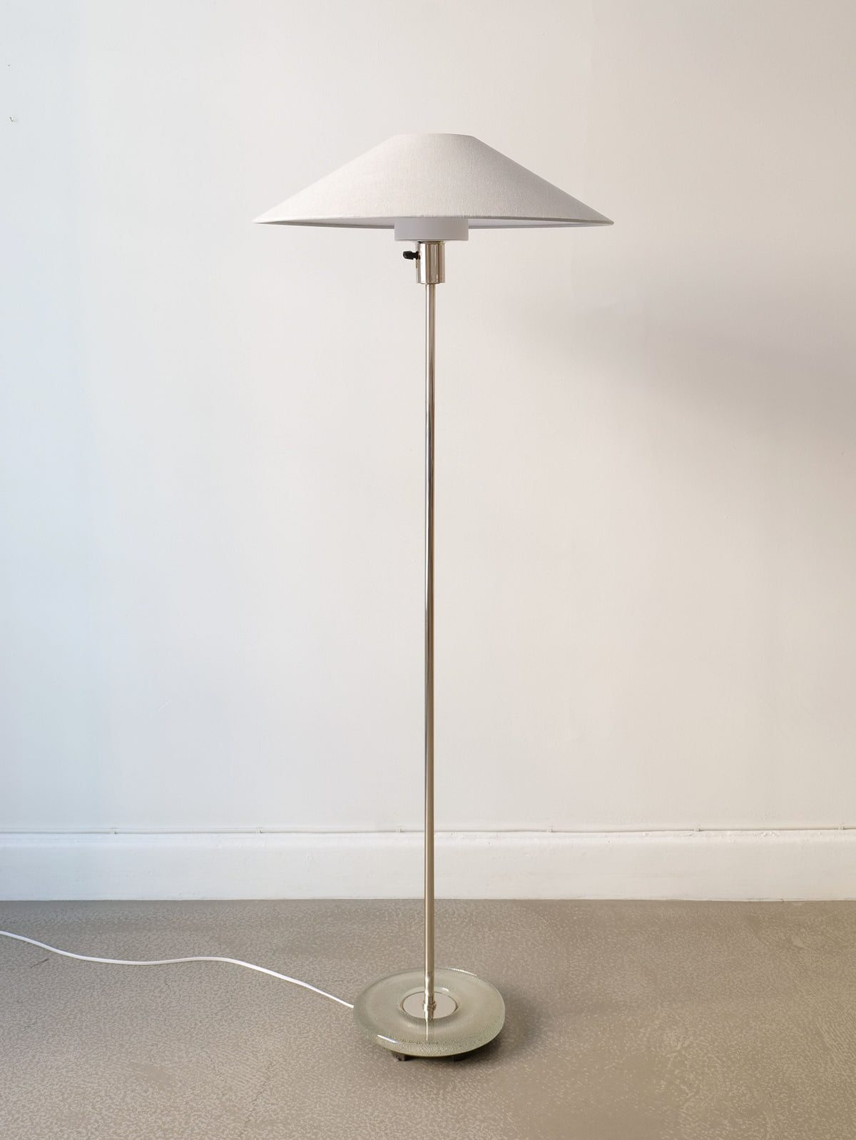 The Deco Floor Lamp Harald Notini 1940s by Collection apart features a white conical shade, slim metallic pole, and round base on a light floor against a white wall, with a white cord extending from the base.