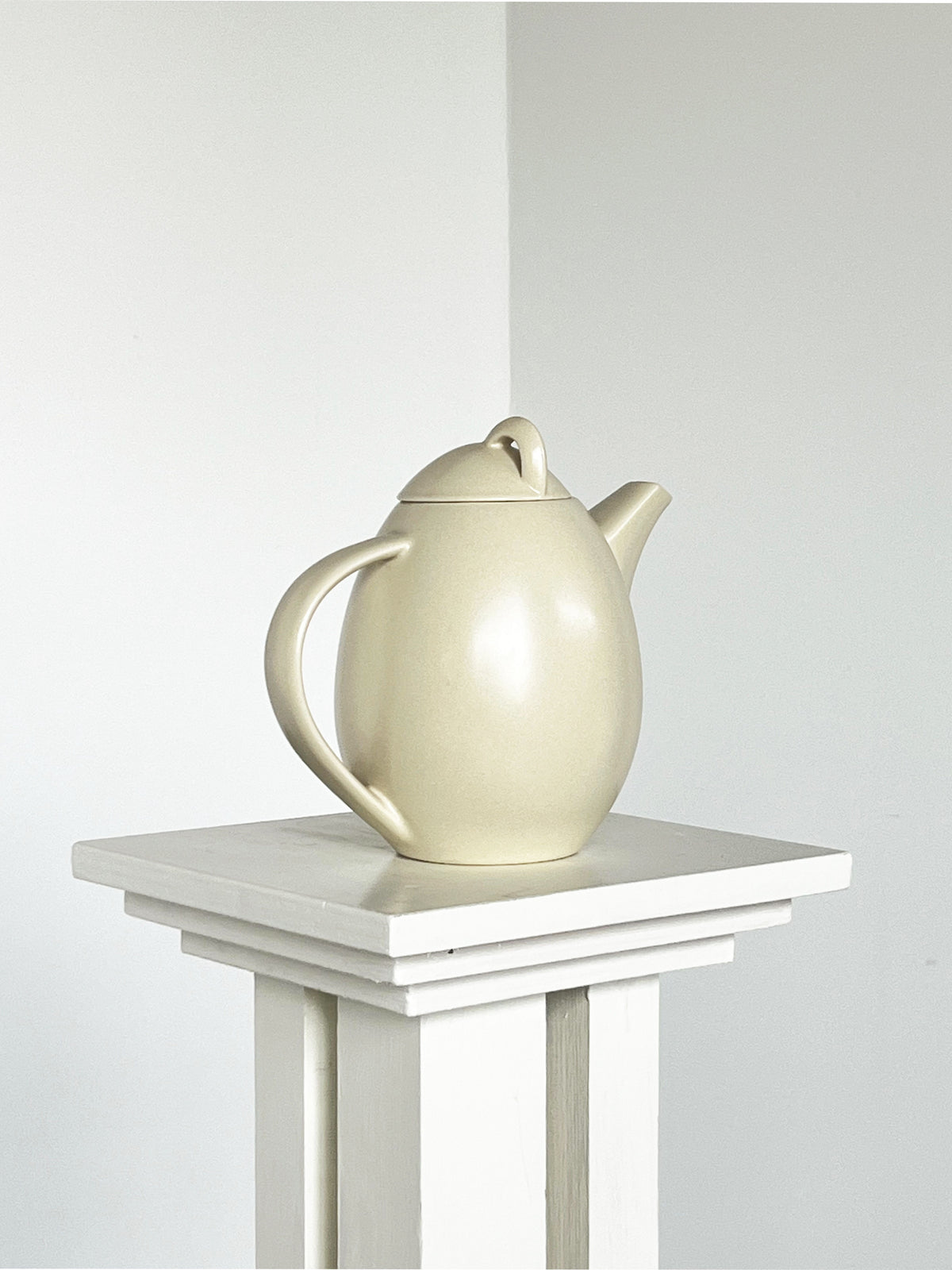 Cream ceramic teapot on white pedestal table, pottery detail
