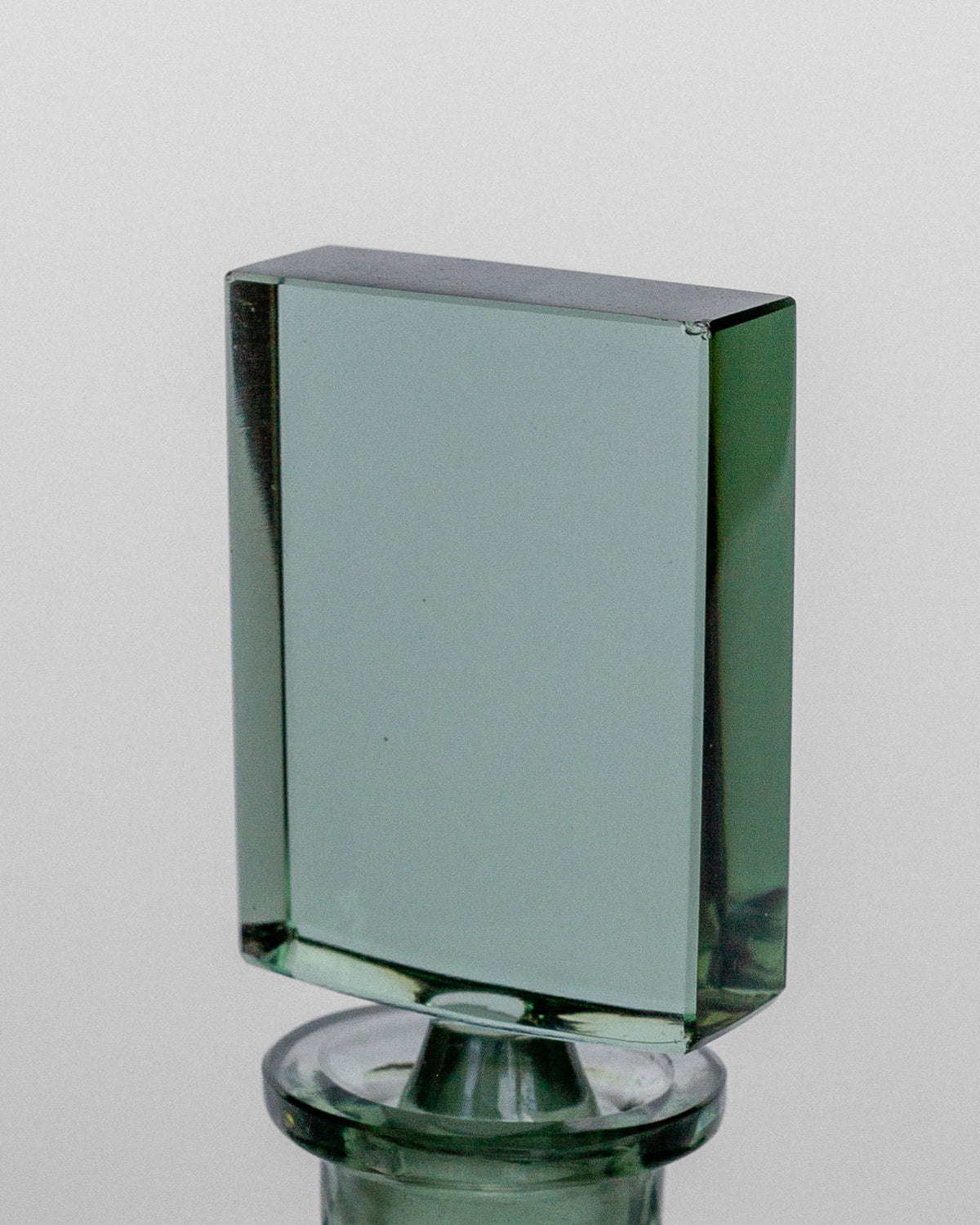 An elegant transparent, rectangular glass block with a slight greenish tint, evocative of the Spigel Art Deco Perfume Bottle from the 1930s Czech collection, stands vertically on a rounded base against a plain white background. The glass has smooth, polished edges and appears to be either a decorative object or a paperweight.