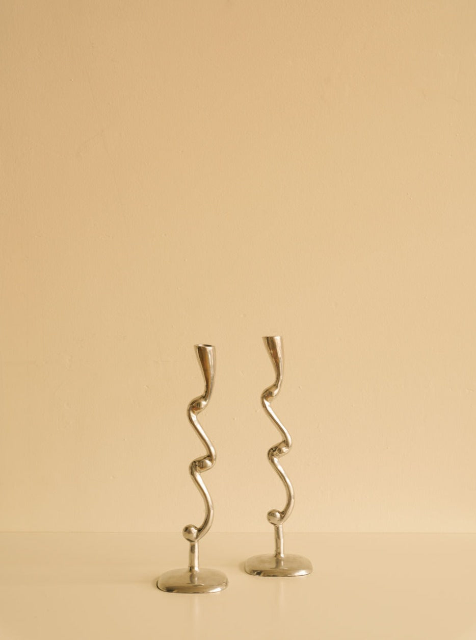 Two Curly Candleholders from Les Objets Amsterdam against a plain beige background.