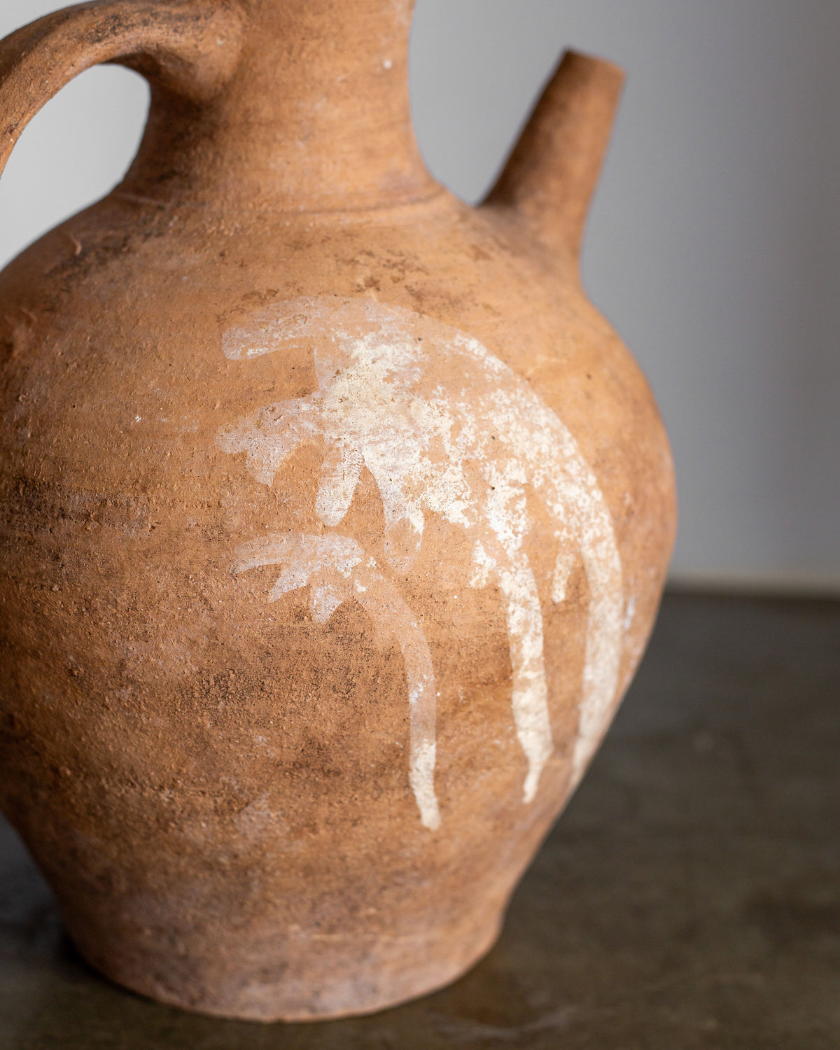 This Early 20th Century European Ceramic Pitcher by Spigel is a hand-crafted rustic jug featuring a spout, handle, and faded white lion design. With neutral gray tones, it serves as an exquisite decorative piece and a timeless testament to artisan craftsmanship.