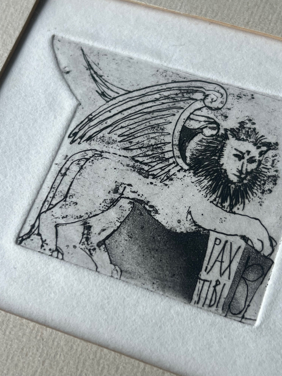 A framed and mounted product by Porter Studio featuring an oak-framed black and white etching of a winged lion with a mane, surrounded by a textured mat. The right side displays a Latin hand illustration with the text "PAX TIBI.
