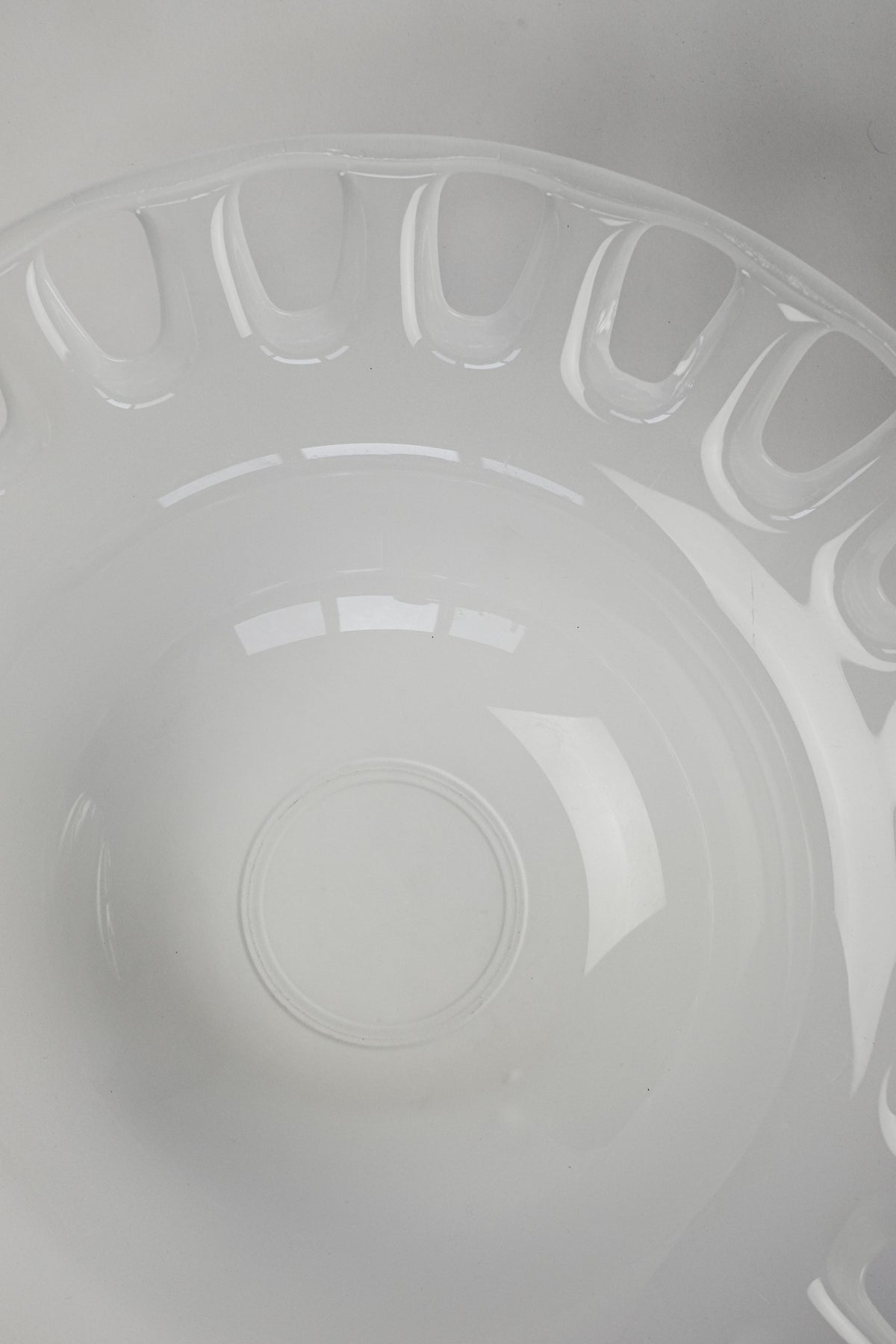A close-up of septembre studios' Large Bowl of Milk Glass in white, featuring a smooth circular design with a glossy finish. Its reflective surface shows a faint window reflection against a soft gray background.