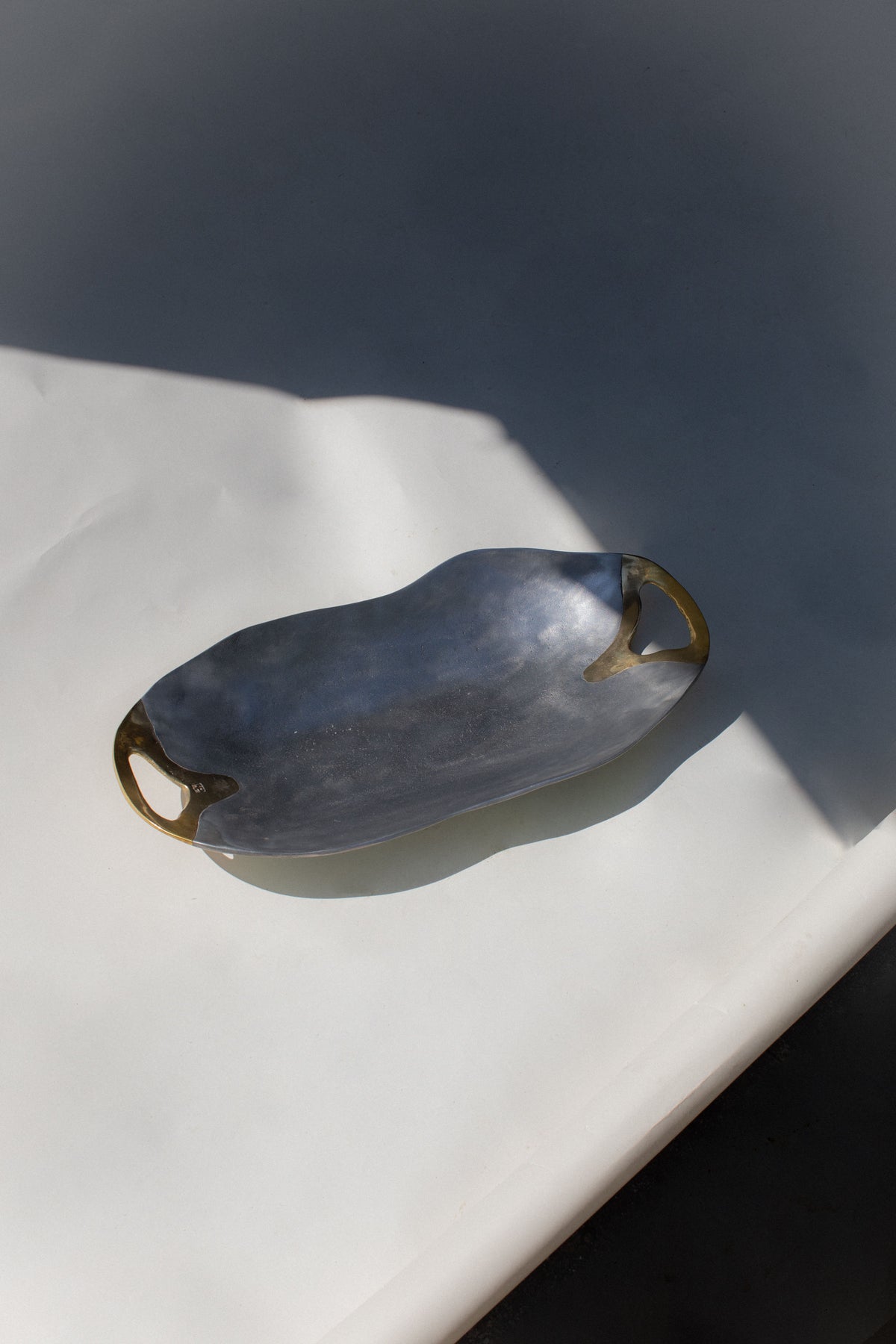 Gray brutalist ceramic bowl with curved handles on white marble surface