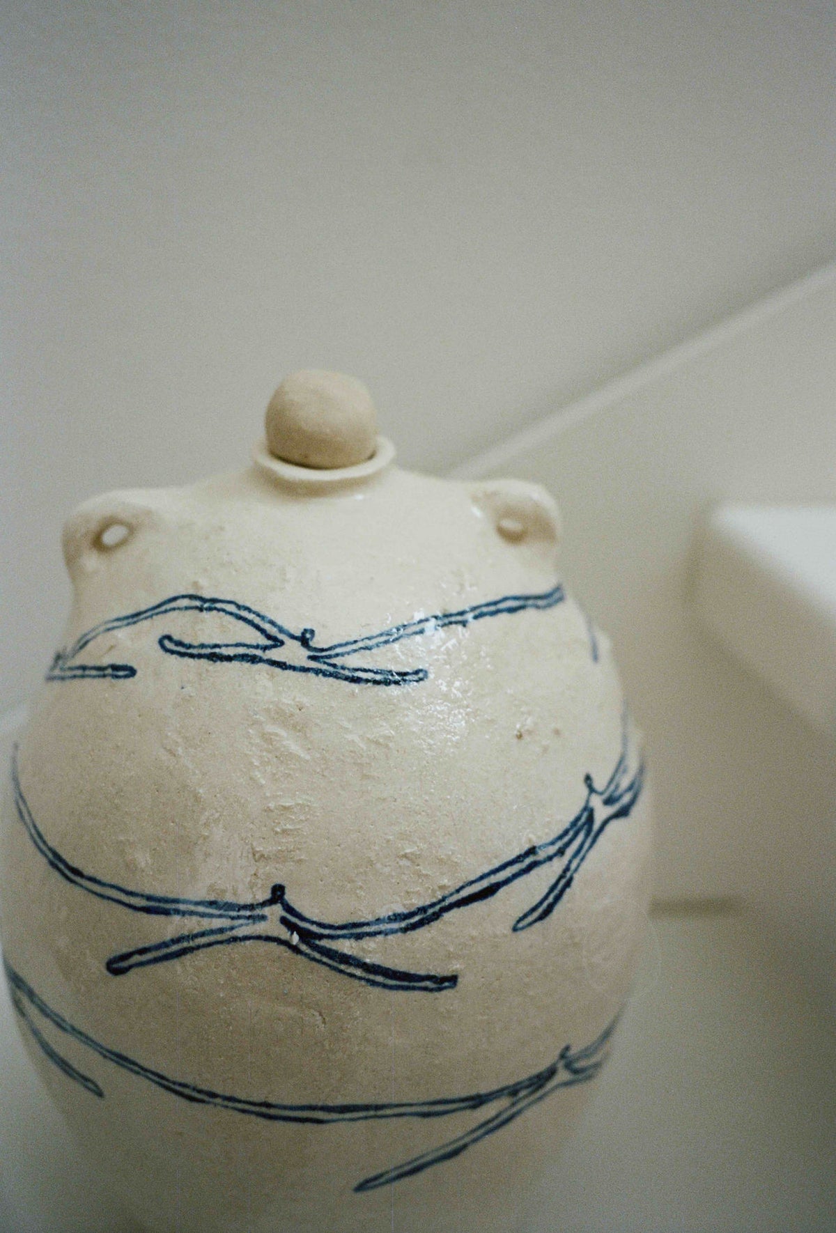 The ATELIER1991 'Ladies Holding Hands' Ceramic Vase, featuring a cream glaze, blue dragonfly patterns, and Persian-inspired motifs, sits on a white surface against a pale background.