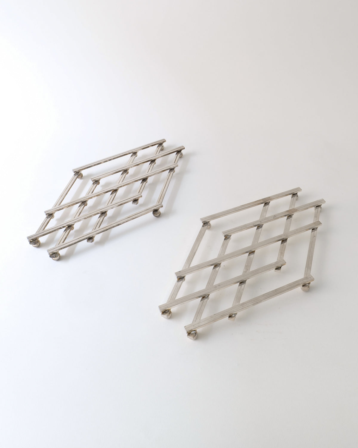 Two silver metal expandable trivets with grid pattern from 1950s
