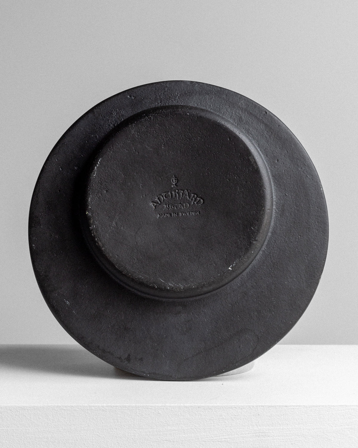 The Cast Iron Zodiac Dish by Spigel is showcased on a white surface, featuring a gray, round, vintage design with embossed text and a small central emblem that may represent a zodiac motif.
