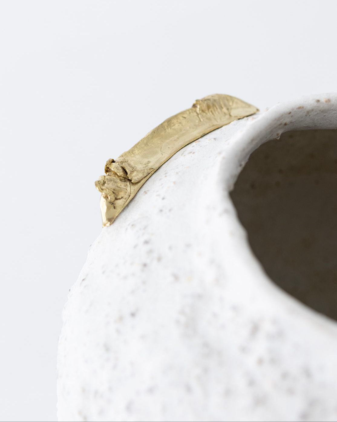 Close-up detail of bone-white ceramic vase with golden accent