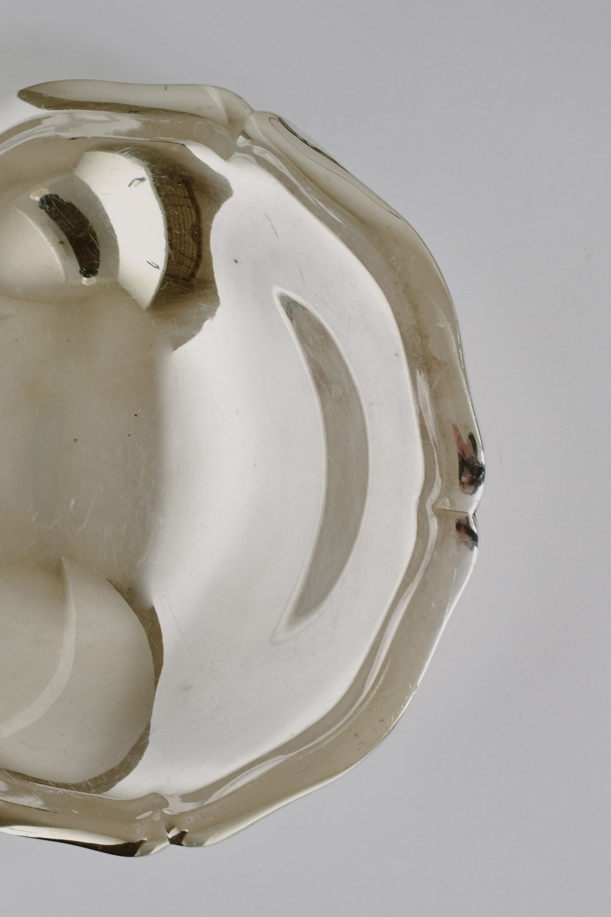 A shiny, reflective Silverplated Bowl by septembre studios with curved edges is shown against a plain background. The surface of the bowl captures faint reflections, enhancing its unique character. The top right section of the bowl is visible.