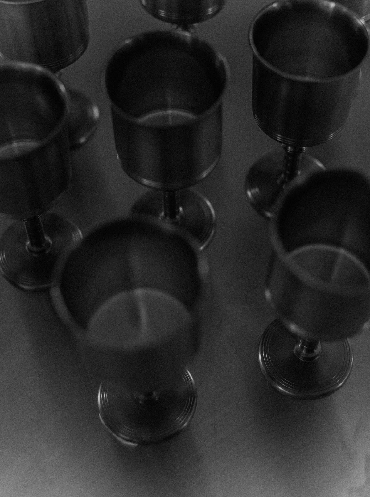 A black-and-white photo of several empty, Out For Lunch Art Deco Cups arranged on a flat surface. The cups are evenly spaced, casting soft shadows beneath them. The overall lighting is dim, creating a somber and reflective mood that embodies timeless elegance.