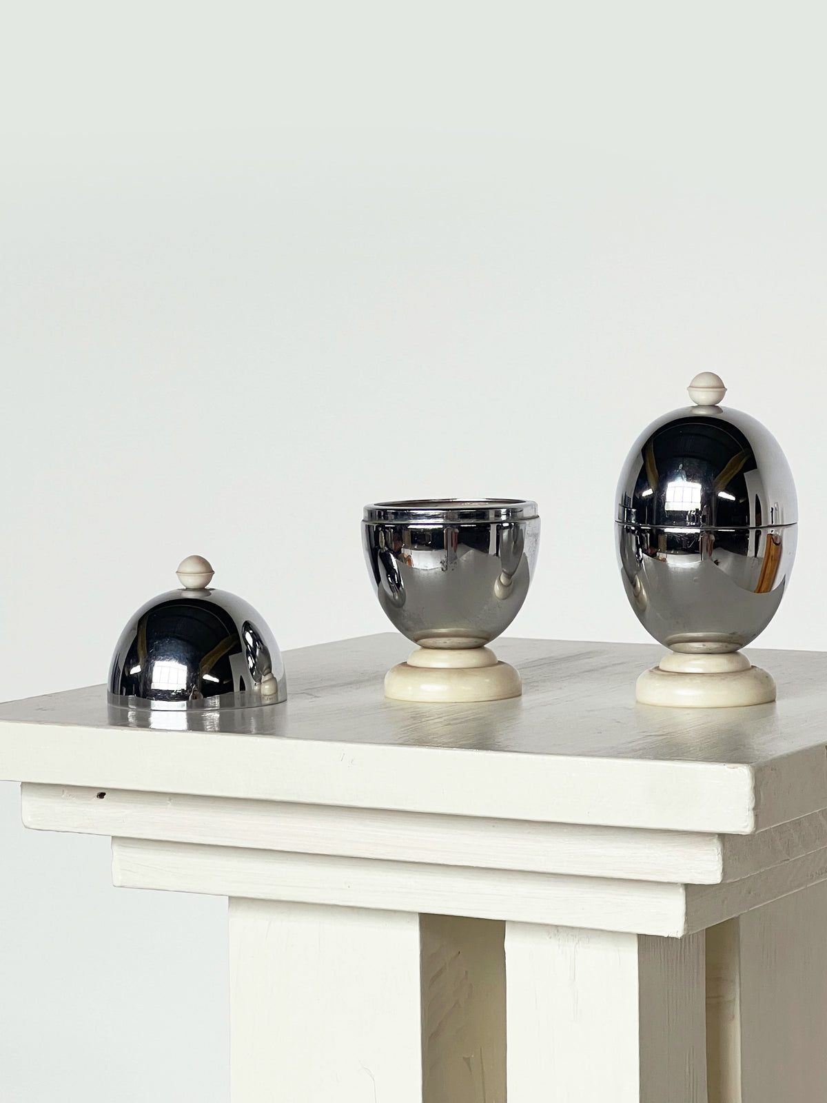 Chrome egg warmers with ivory bases on white wooden table