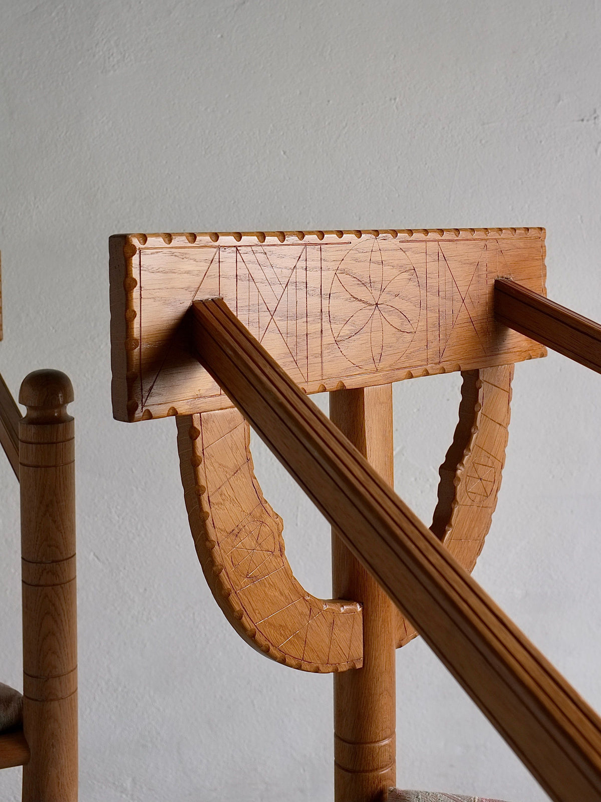 Close-up of a wooden handrail with intricate carved designs, supported by an ornate wooden post. The handrail features geometric patterns, while the post has semi-circle carvings and horizontal grooves. Echoing the Sweden Design period 1950s, it complements Veter Vintage's Rustic Carved Oak Corner Chairs nearby.