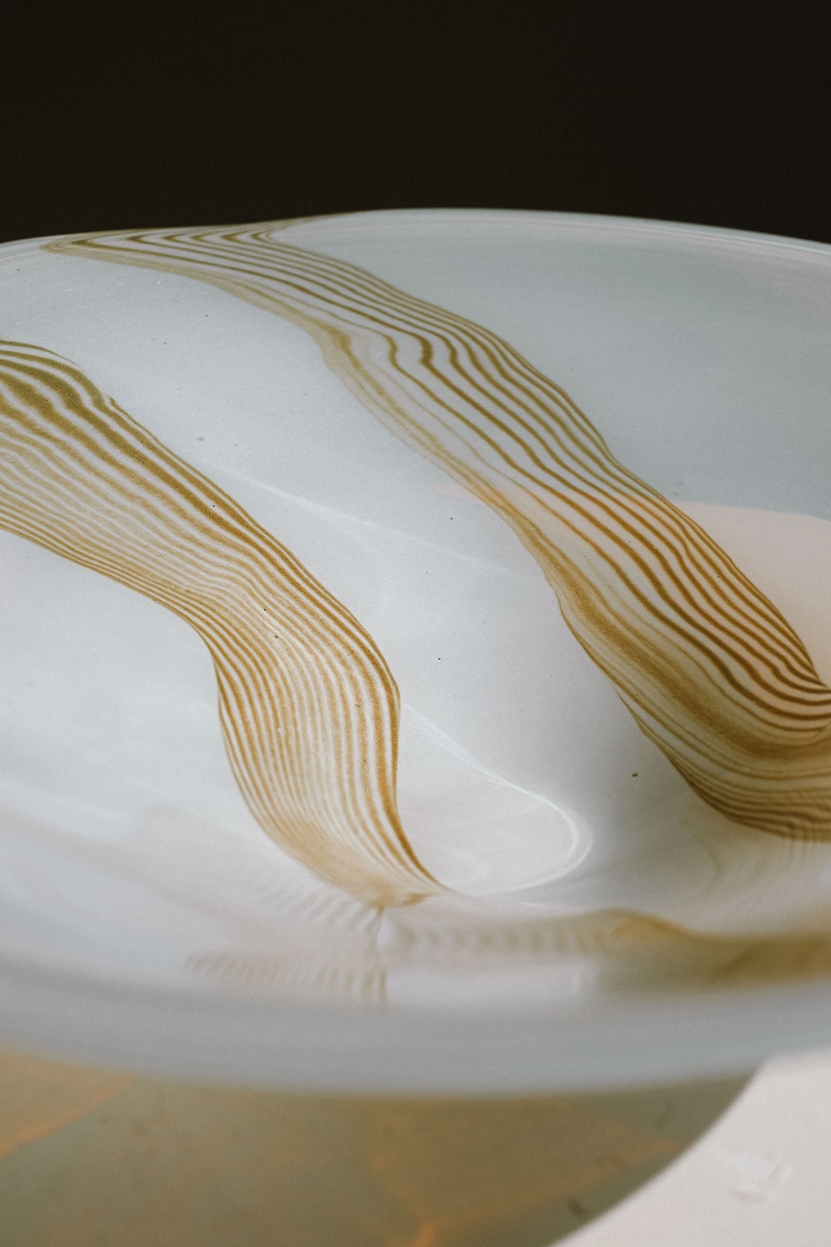 Flowing amber striations detail on white blown glass bowl surface