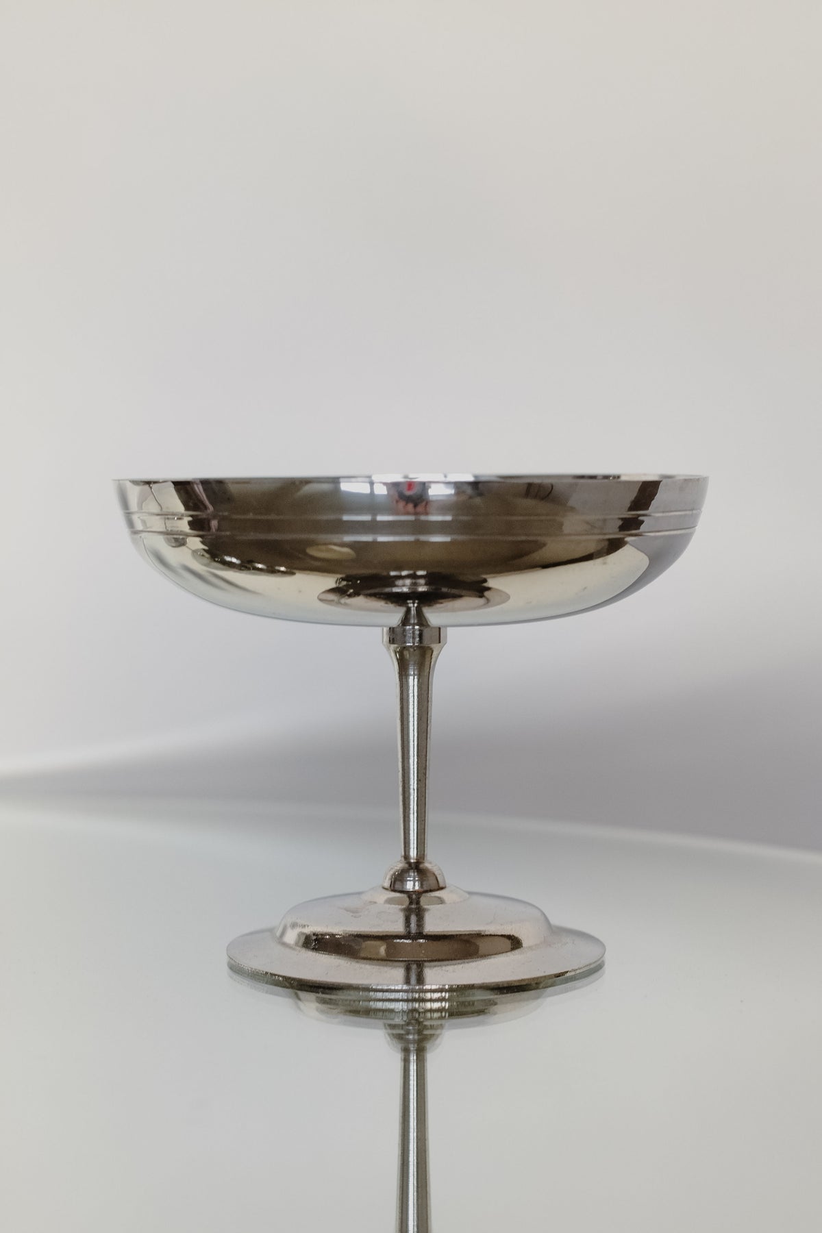 Centered against a plain, light background is a sleek stainless steel pedestal bowl from the "Set of four Ice Coupes" by septembre studios. Its reflective surface and elegant design make it perfect for serving ice cream.