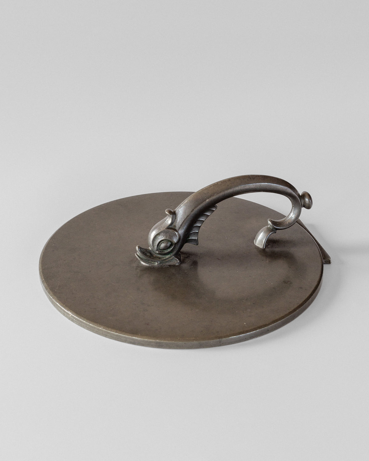 This round metal mirror from Spigel features a decorative fish-shaped handle with intricate fins and scales, reminiscent of an elegant C.G. Hallberg design against a plain background, evoking a vintage feel.