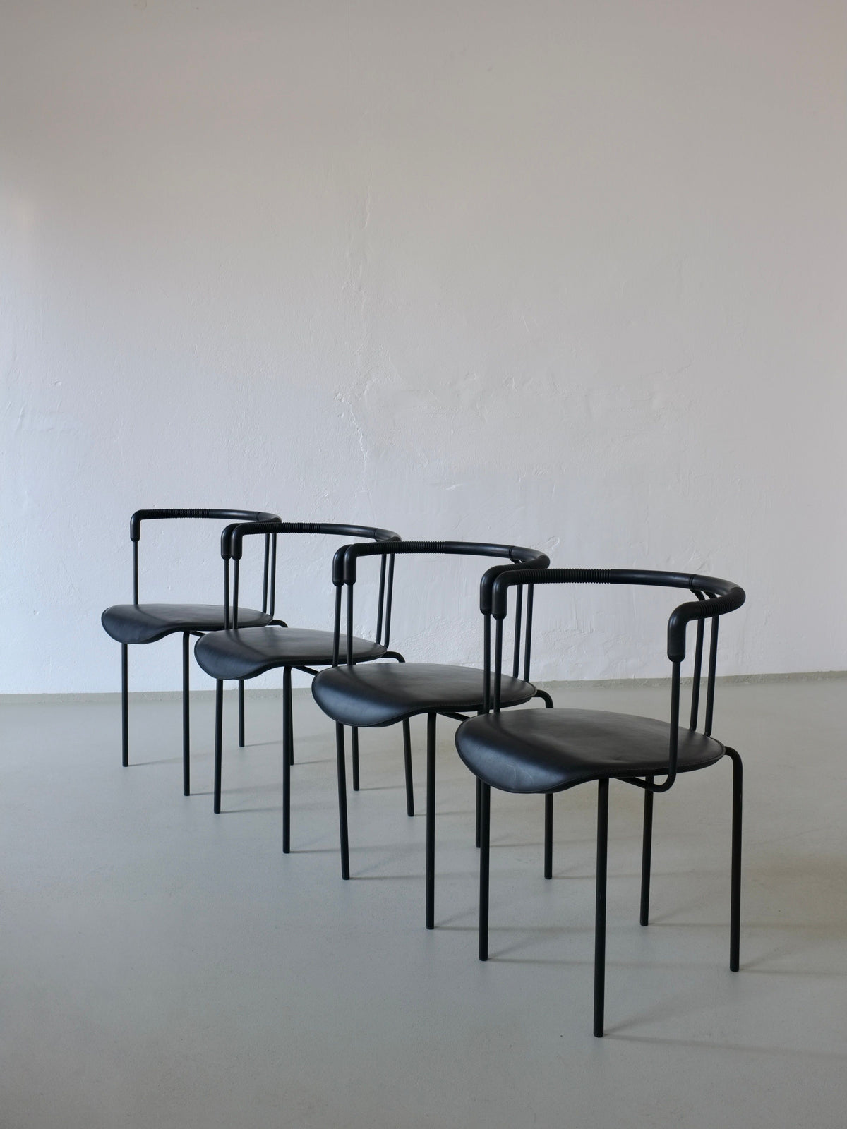 Four black leather Cidue armchairs arranged in minimalist setting