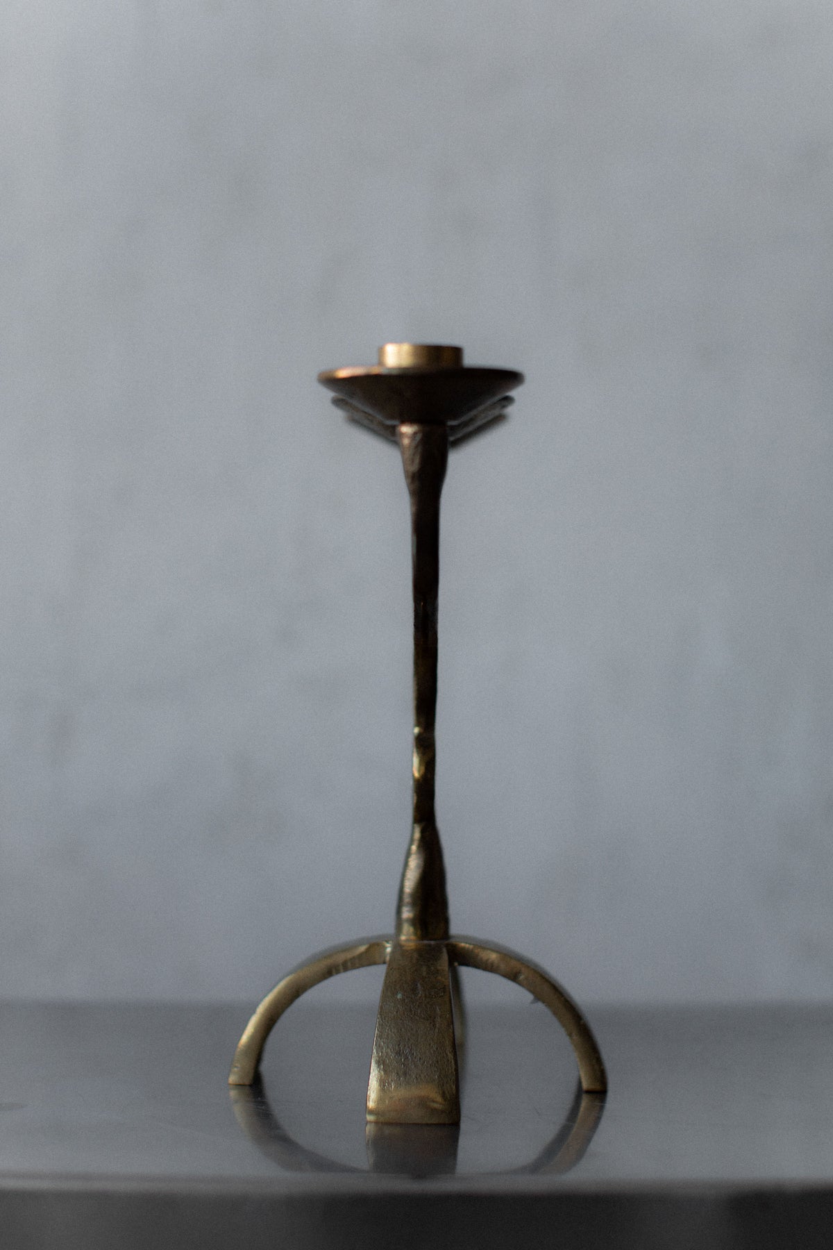 A Brutalist Brass Candleholder by Out For Lunch, showcased on a light gray background, highlights artisanal craftsmanship. It features a simple, slender design with a wide base, capturing a vintage aesthetic.