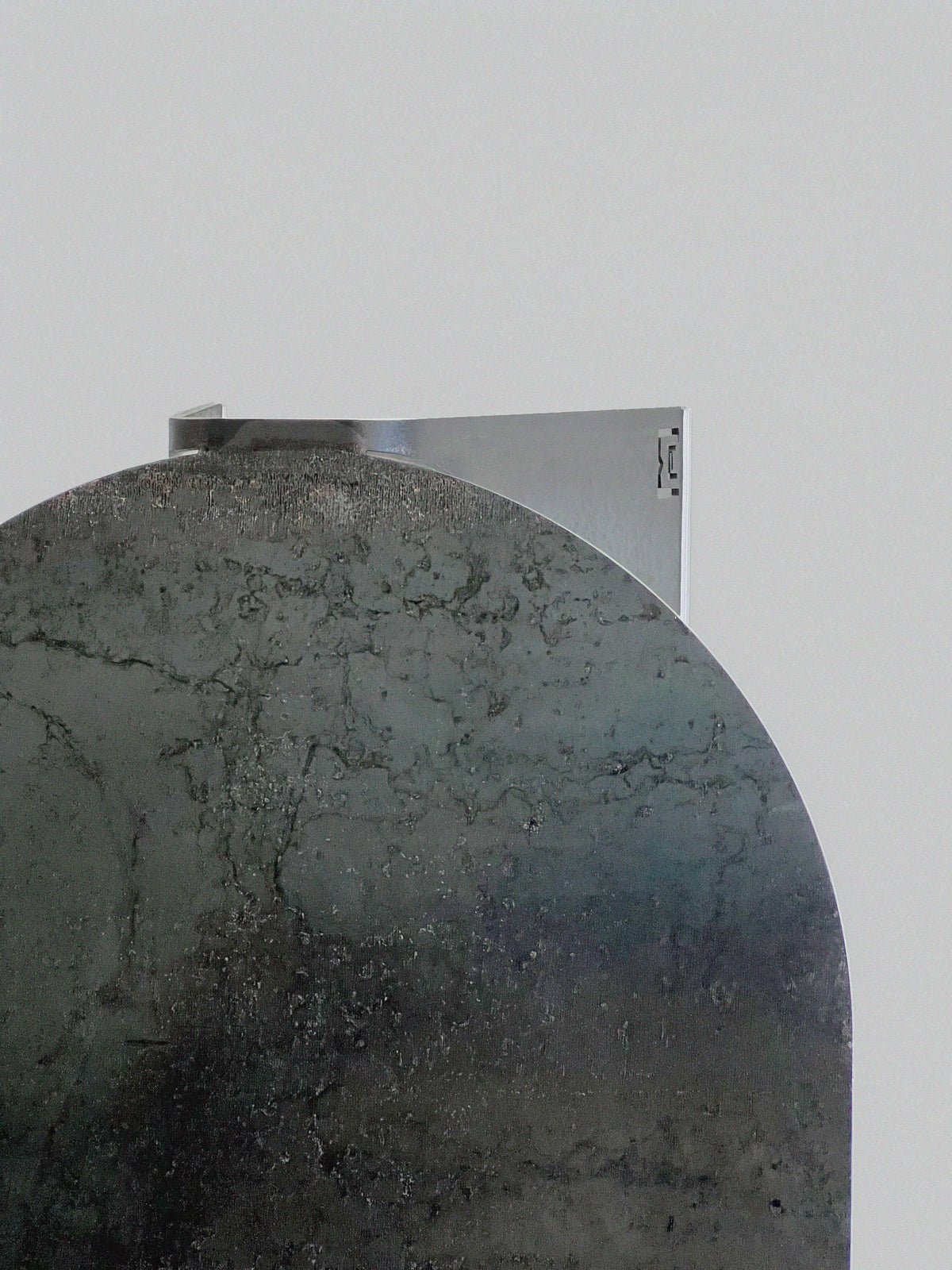 A close-up of two overlapping metal surfaces—curved and textured in front, flat and smooth behind—set against a light gray background, capturing the sleek design inspiration behind the 'Tani' Coffee Table by Modan.