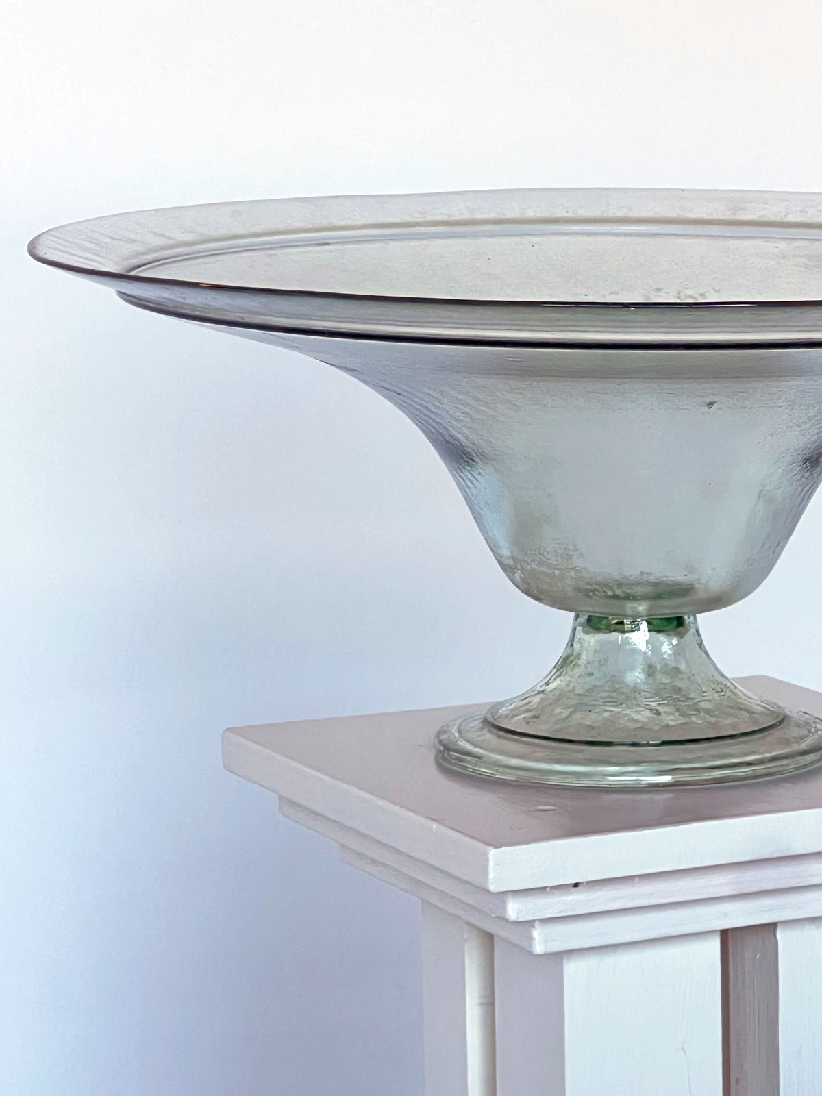 Clear glass pedestal compote bowl with wide rim on white stand