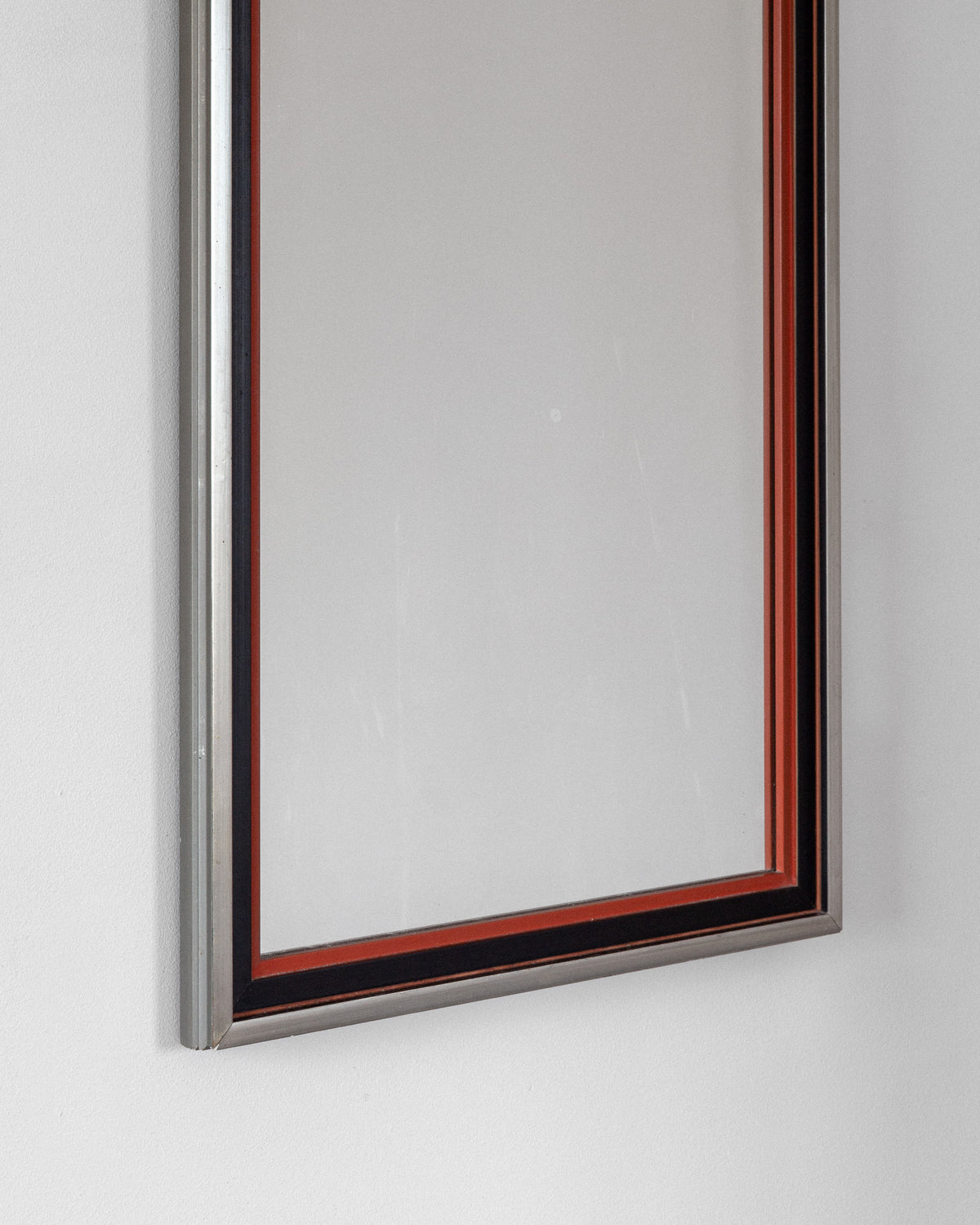A Spigel Art Deco Mirror from 1930s Sweden, featuring a silver and black frame with a red line accent, adorns a plain white wall reflecting the empty space.