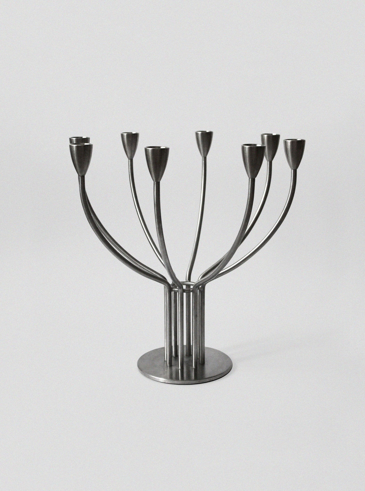 The Brushed Metal Swedish Candelholder by Vintage Stories features seven curved arms and a round base in a minimalist Scandinavian design, perfect for modern décor.