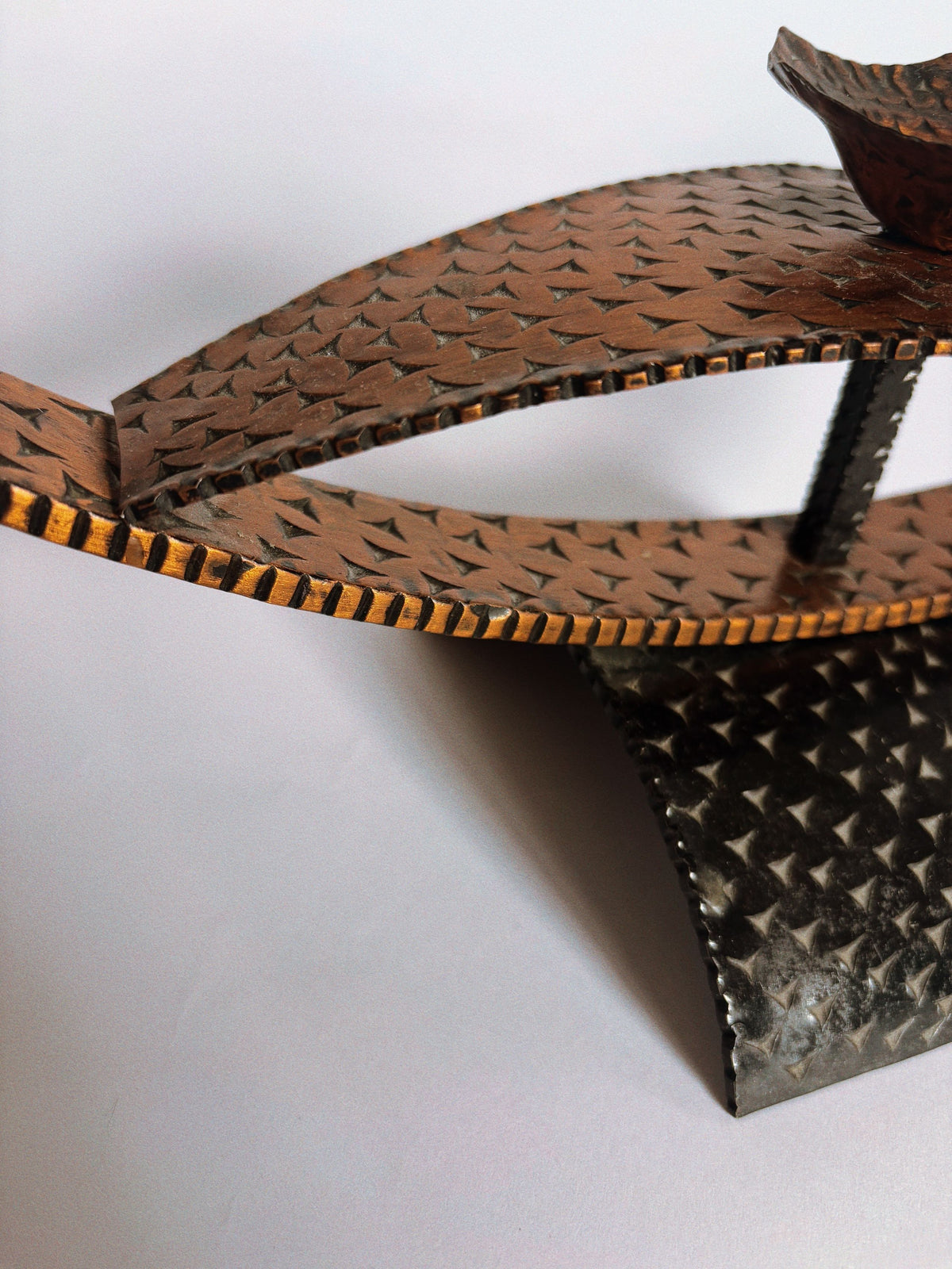 Close-up of Huerto's Two Tone Metal Candleholders featuring curved, textured bronze and black surfaces with geometric patterns and intersecting shapes, reminiscent of a handmade sculpture, set against a light background.