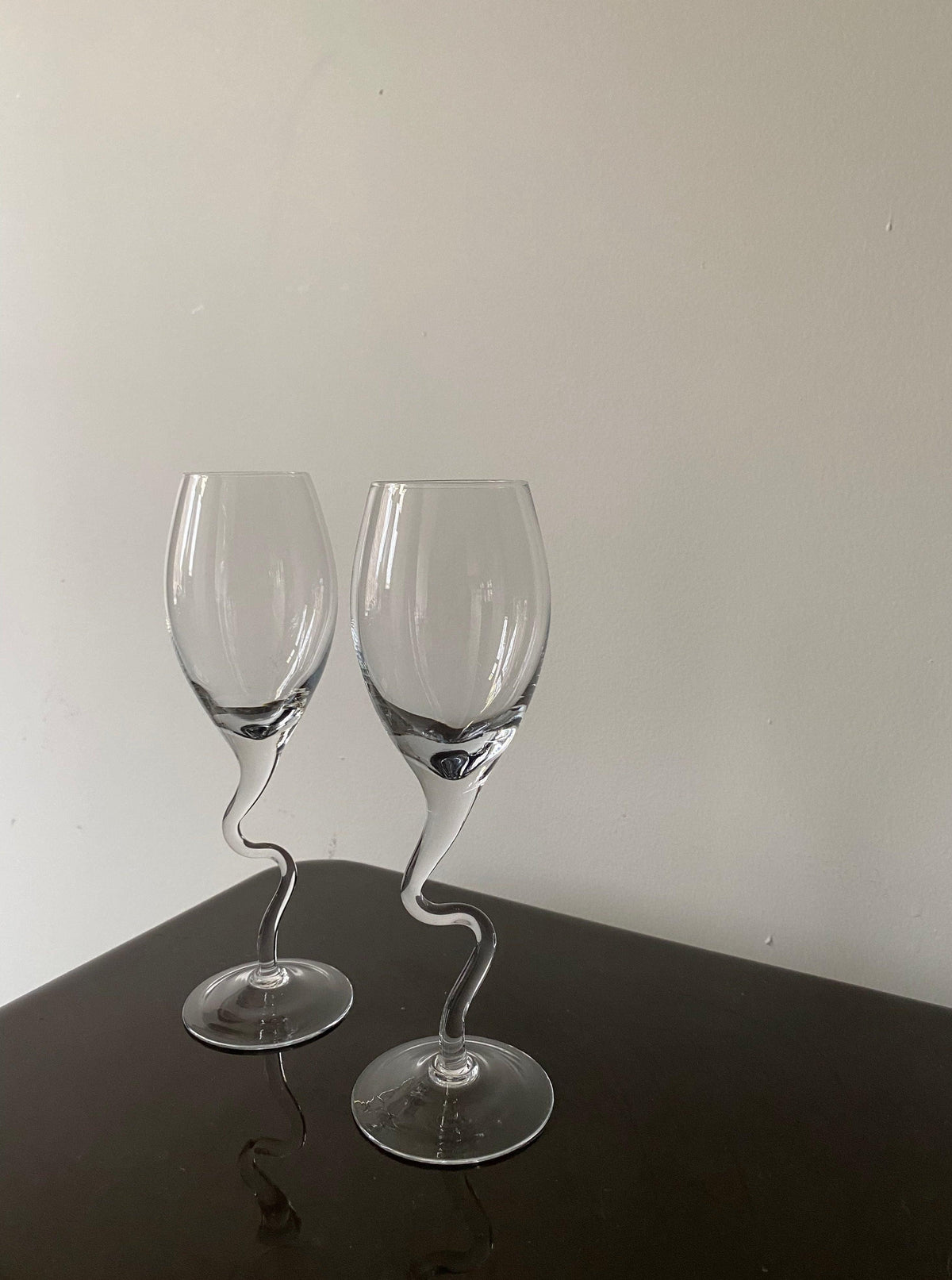 Two elegant Set of Vintage 80s Champagne Glasses with twisted stems by Les Objets Amsterdam on a dark table against a light grey background, perfect for a sophisticated drinking experience.