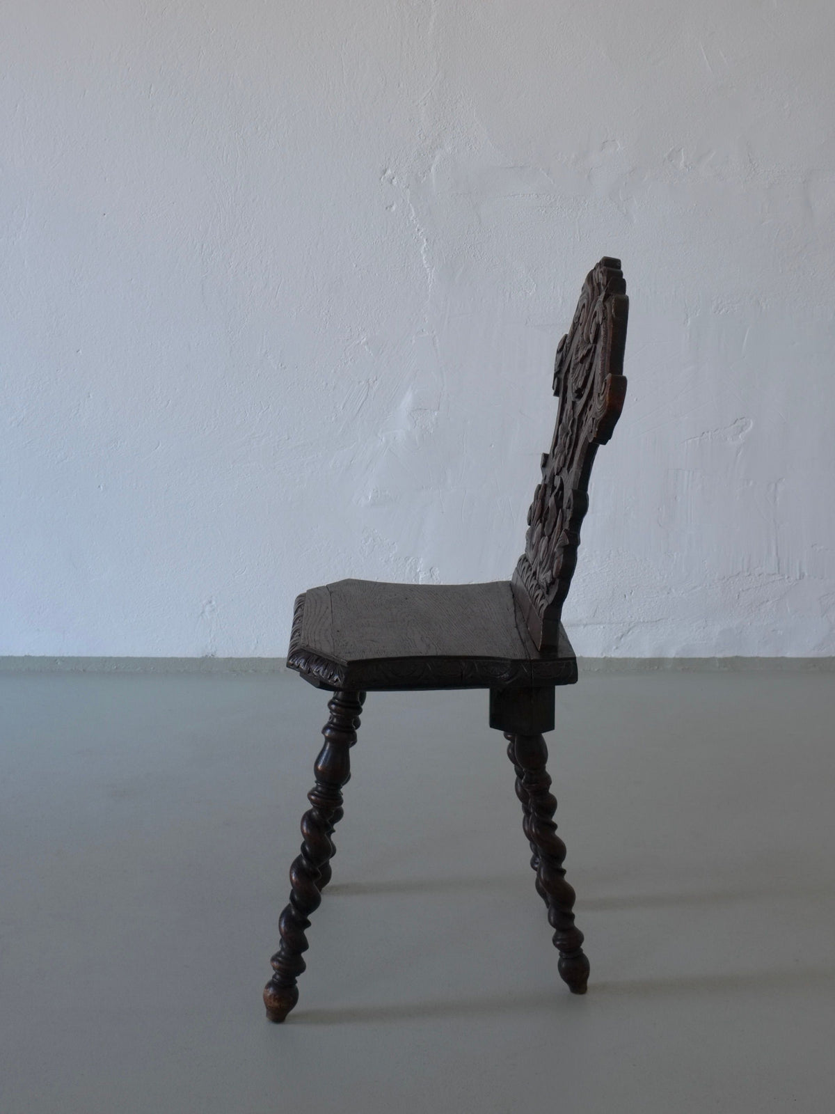 Dark oak chair with carved backrest and twisted legs, side profile view