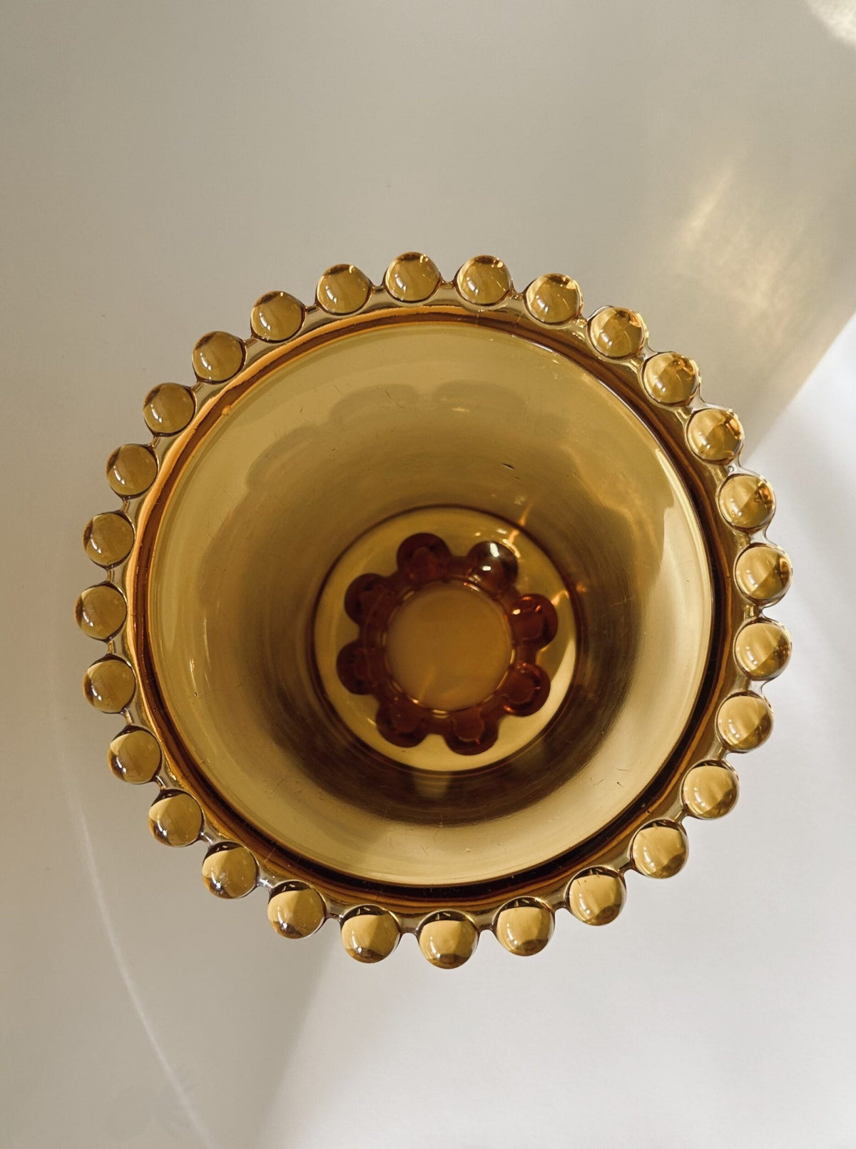 A top-down view of the Art Deco Amber Glass Vase by Rudolf Schrotter from Flock Studio showcases its decorative rim with circular patterns. Reminiscent of vintage Art Deco design, the base exhibits a flower-like motif. Light reflects off its shiny surface, enhancing its rich color and intricate details, evoking the elegance for which Rudolf Schrotter is renowned.