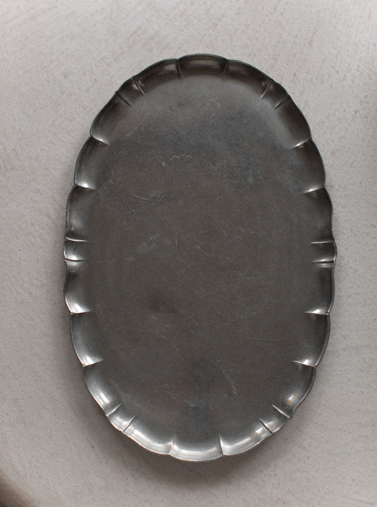 An overhead view of an empty, oval-shaped silver platter with a scalloped rim, placed on a light-colored surface. The Art Deco Swedish Grace Tea-set by Out For Lunch has a slightly tarnished appearance, adding vintage charm and Swedish grace to the minimalist scene.