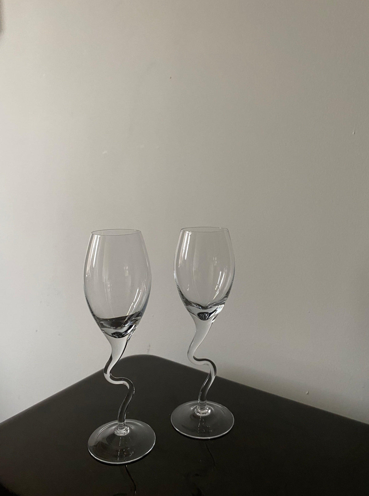 Two empty Les Objets Amsterdam vintage 80s champagne glasses with twisted stems on a dark table against a light gray wall.