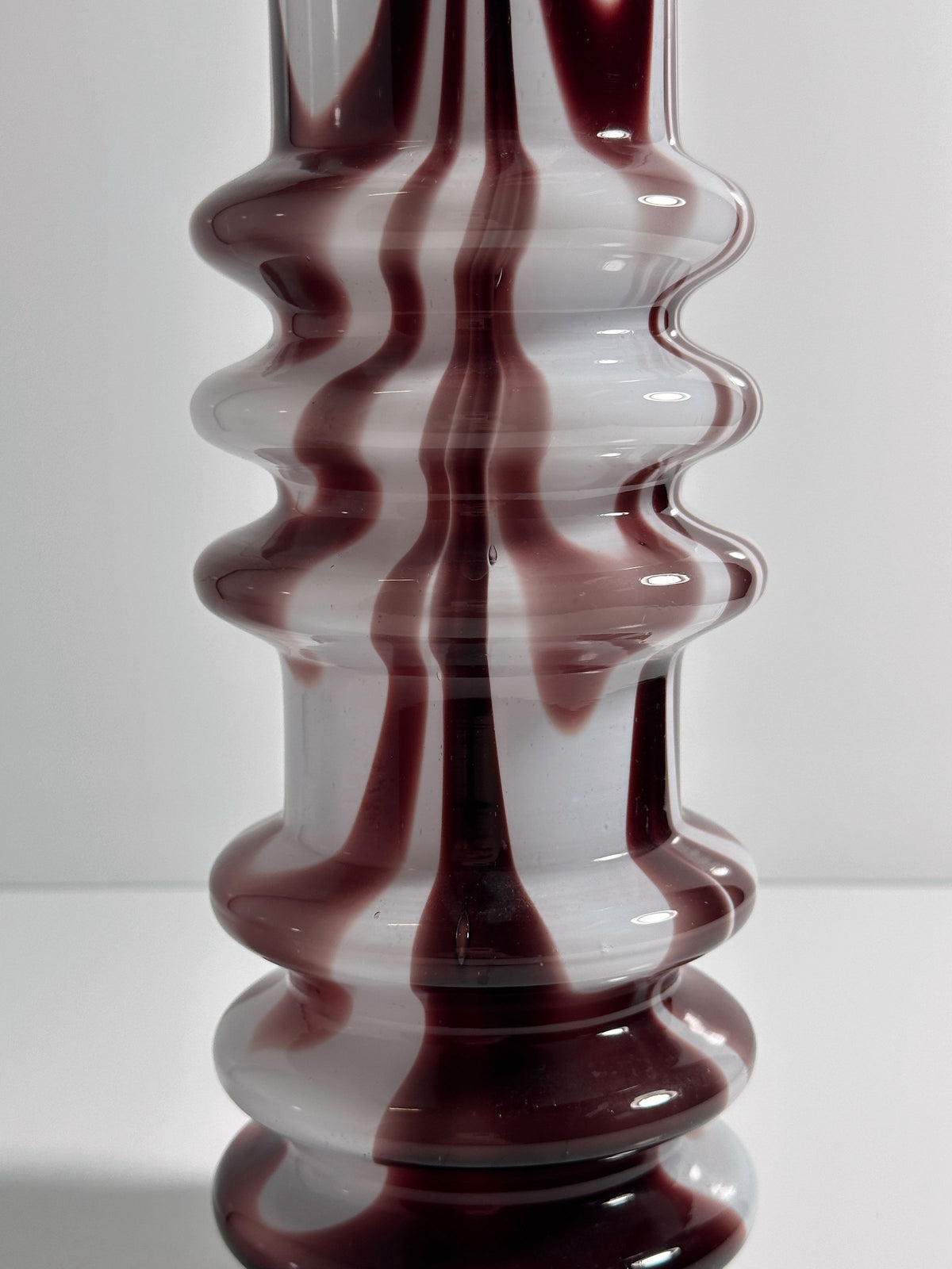 The 1970s Carlo Moretti Opalina Fiorentina Vase by Dodo Vintage displays opal glass with a wavy, ribbed texture and swirling maroon and white patterns, offering a fluid, marbled effect that reflects light gracefully against a plain background.